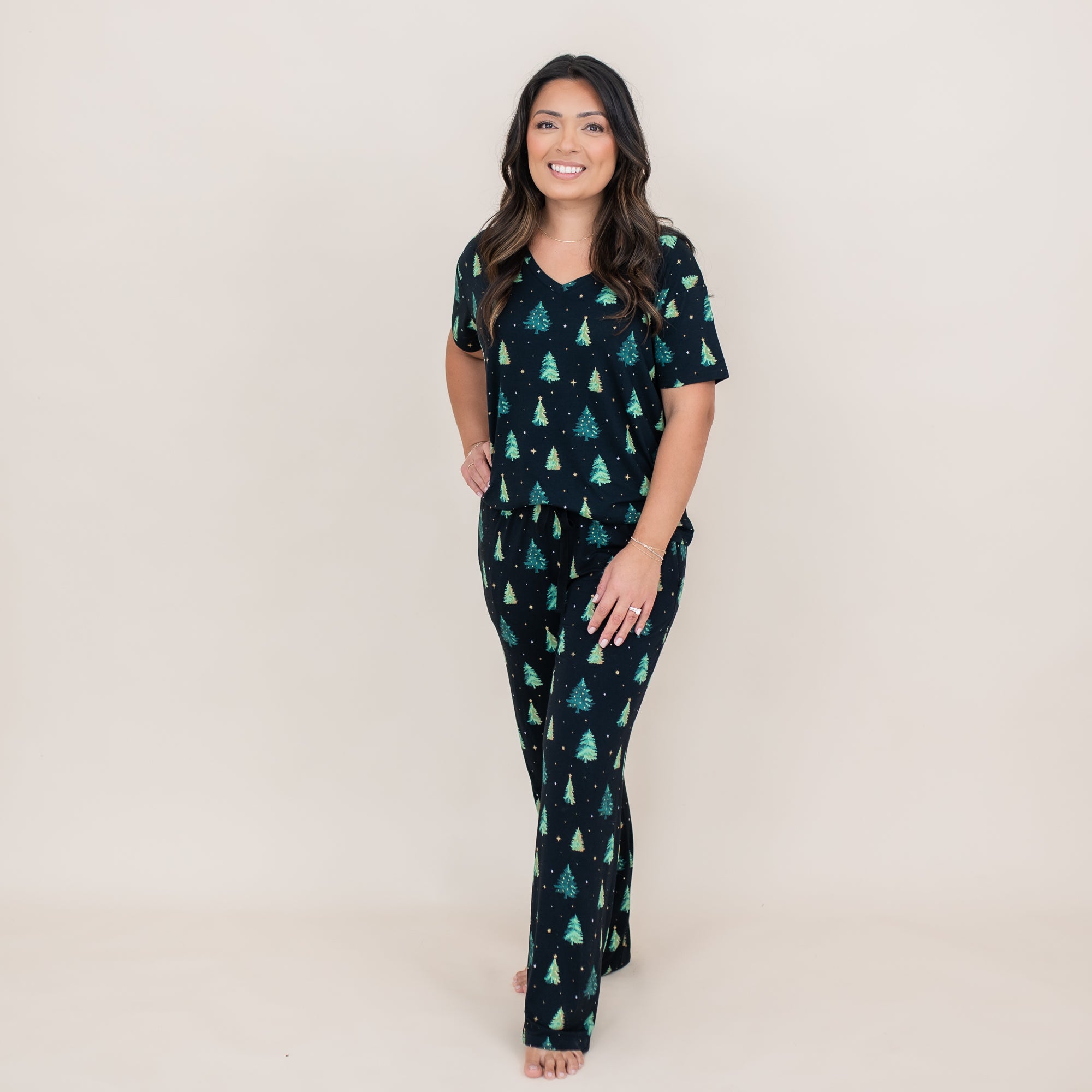 Smiling female standing with on hand on her thigh wearing the Women's Lounge Pants in Twinkle Tree paired with a matching women's V-neck
