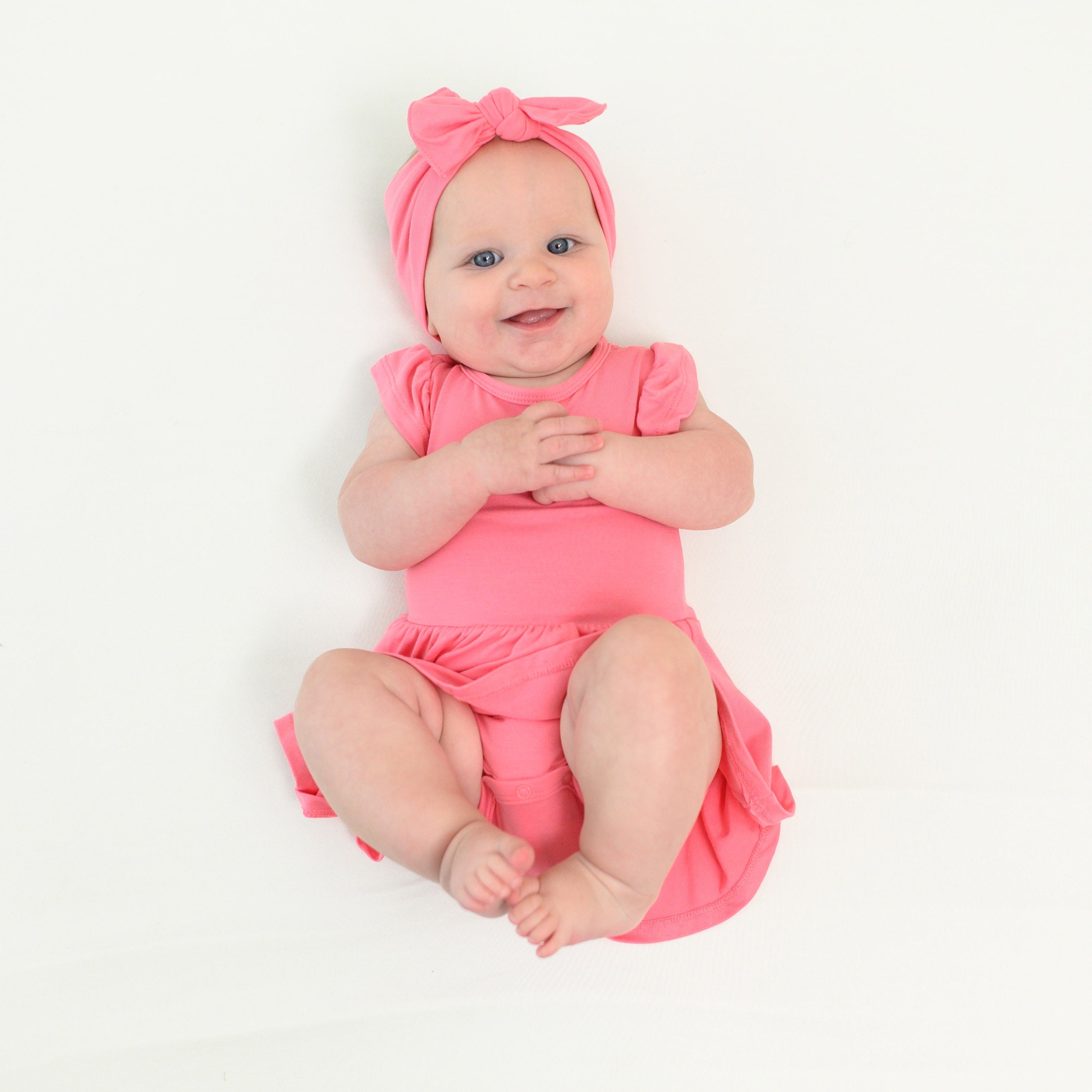 Baby wearing twirl bodysuit Pink Bamboo Dress and Bow Headband in Guava
