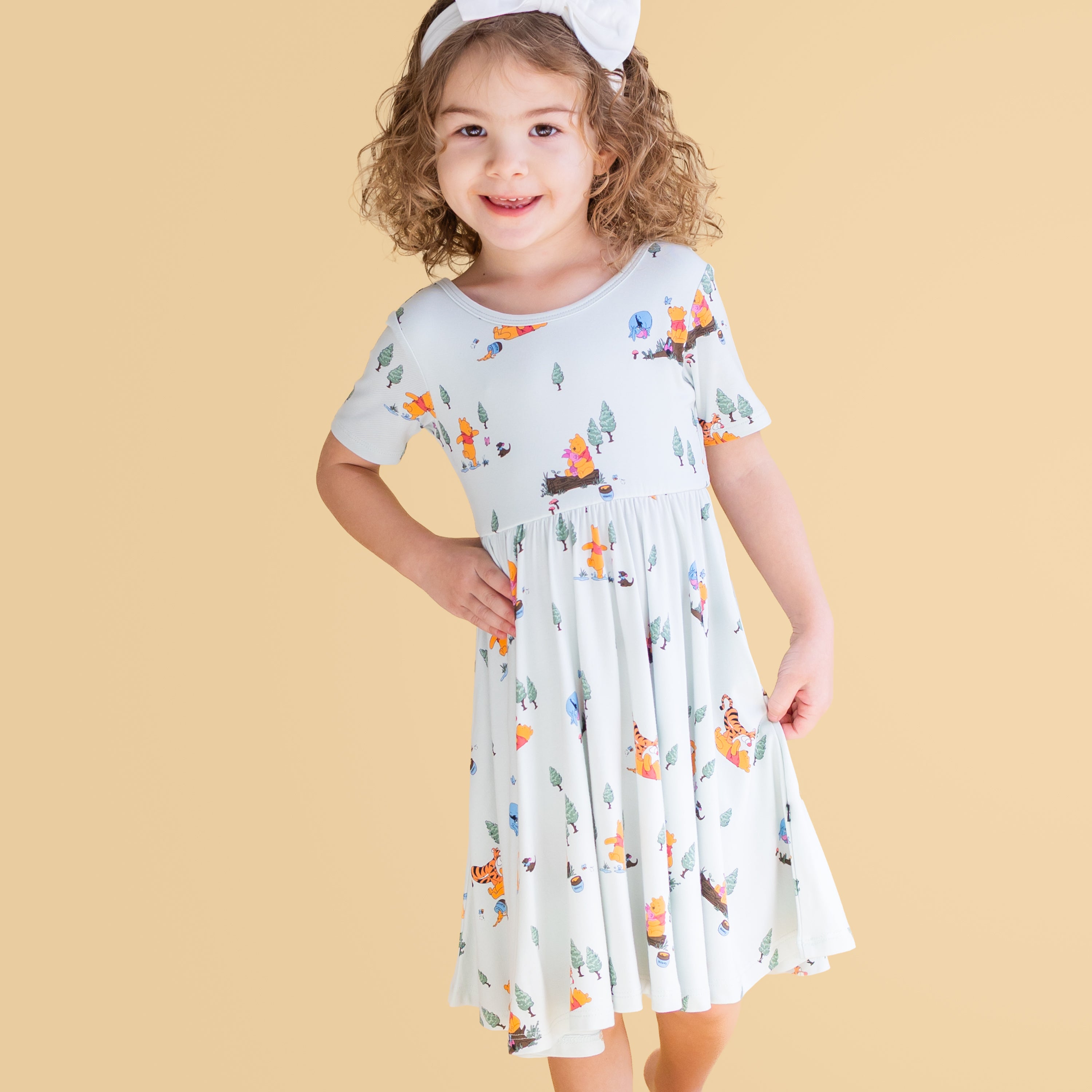 Young girl modeling the Twirl Dress in Winnie the Pooh Hundred Acre Wood with a white bow
