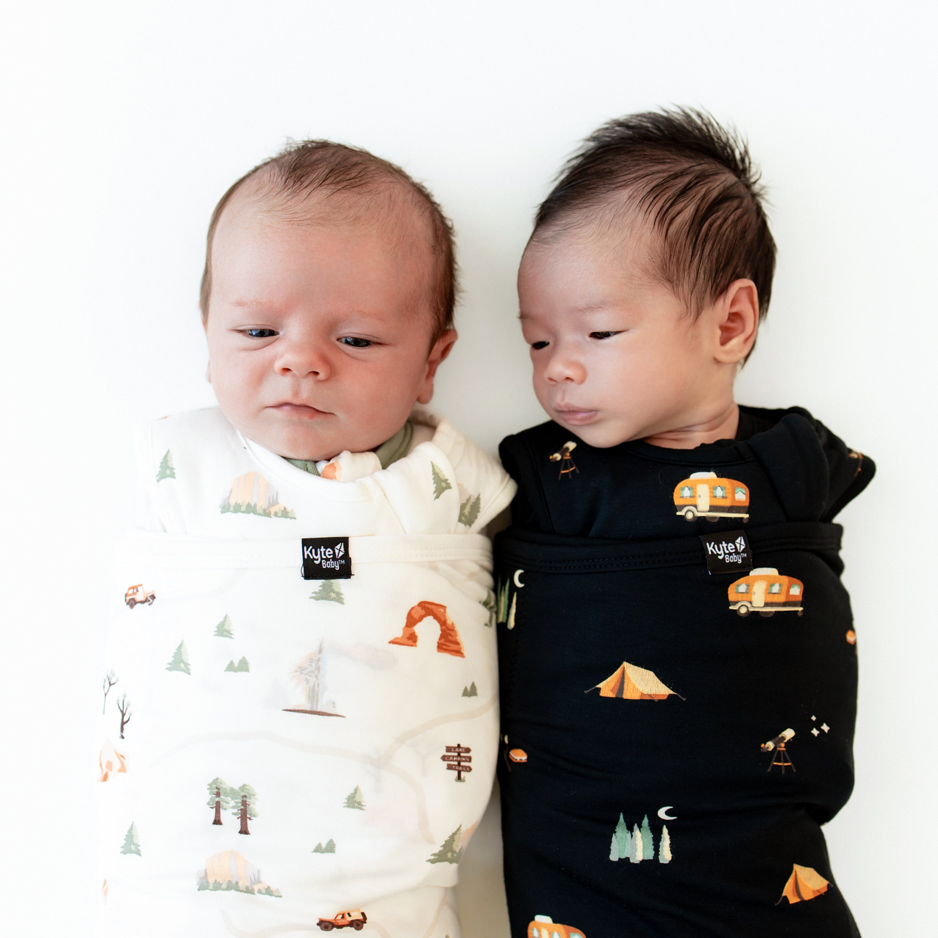 Two newborns laying side by side swaddled in Sleep Bag Swaddler in Under the Stars 1.0 and Road Trip 1.0
