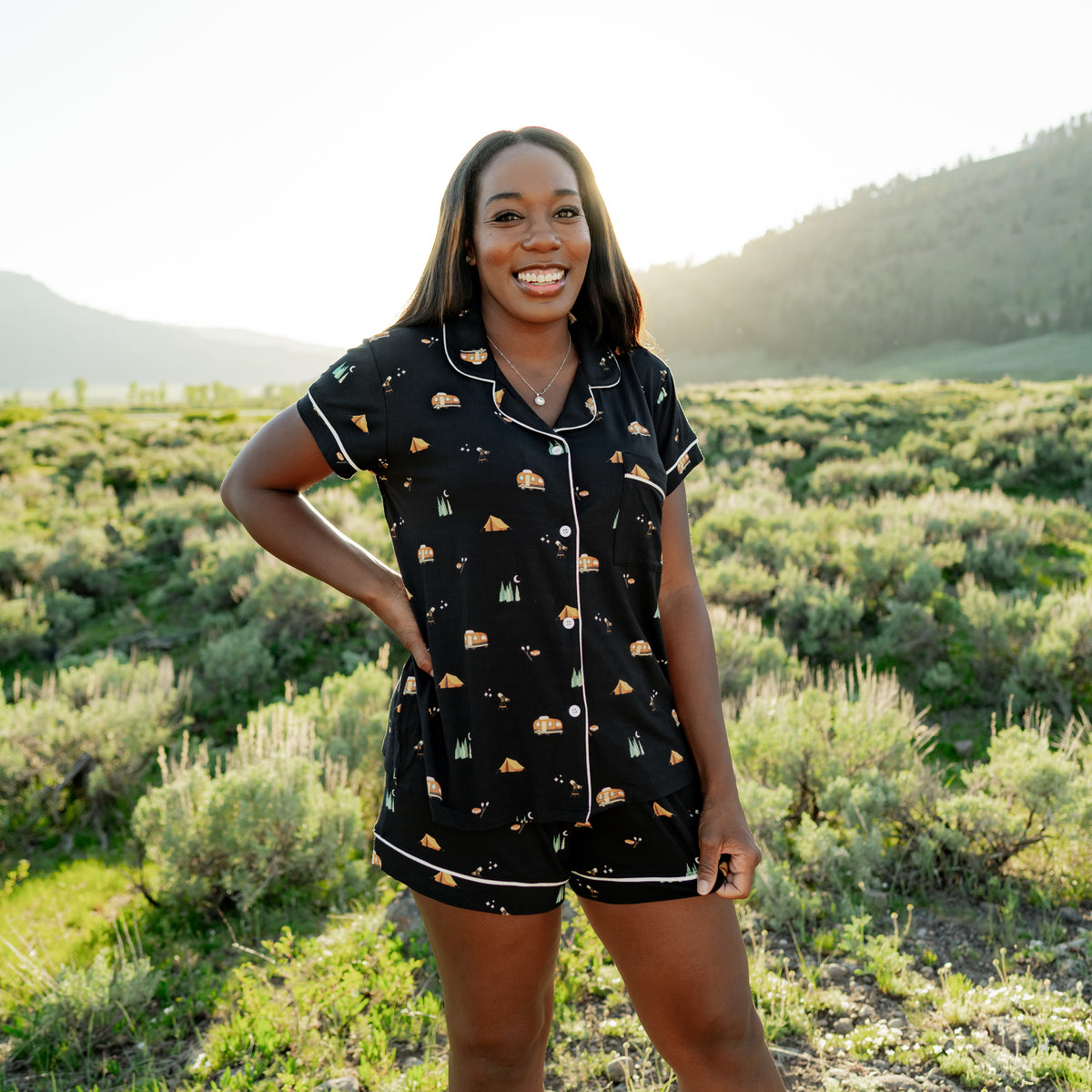 Smiling female model standing in a field in a Montana National Park wearing the Women's Short Sleeve Pajama Set in Under the Stars