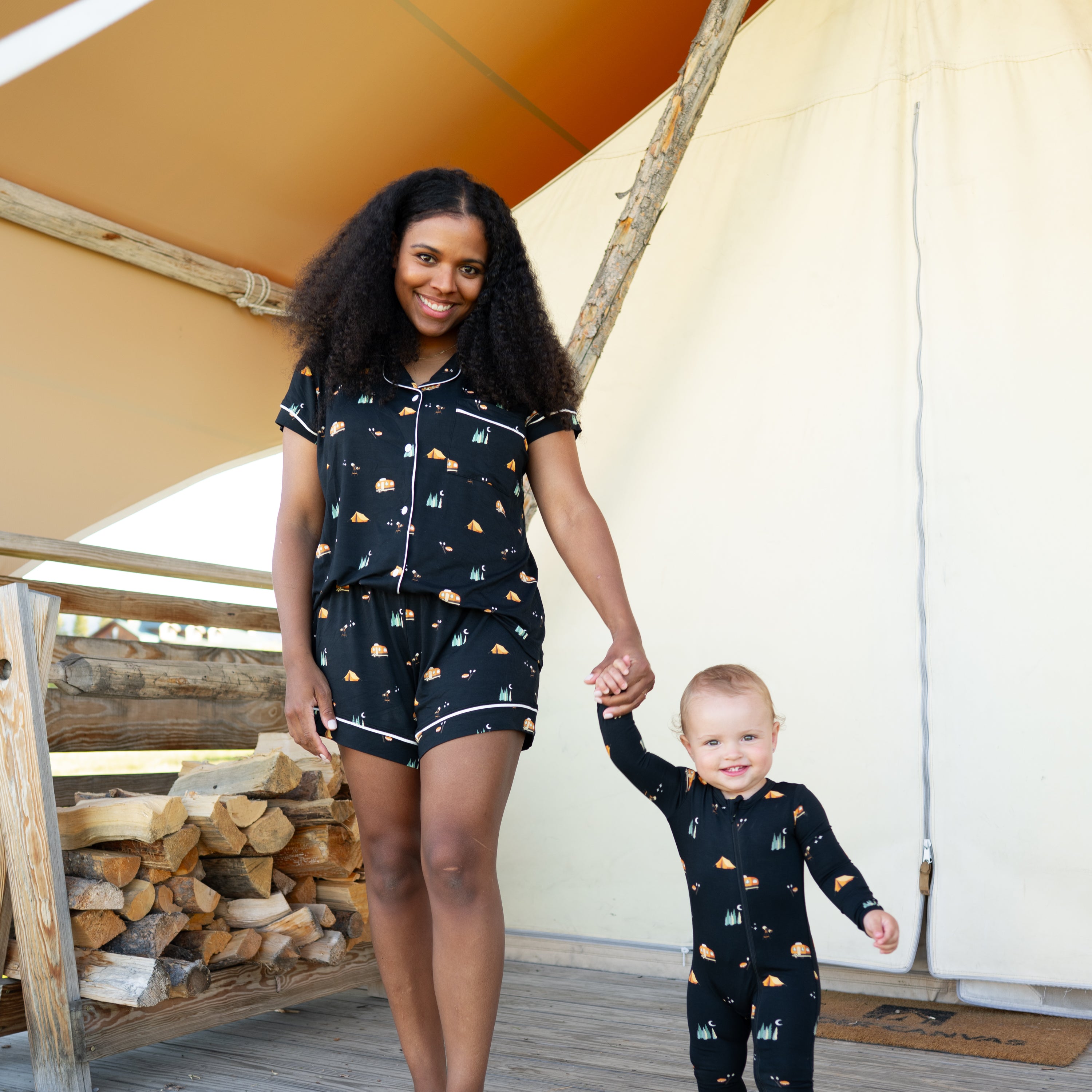 Smiling mother and child holding hands matching in Under the Stars. Mother is wearing the Women's Short Sleeve Pajama Set and child is wearing a zippered romper