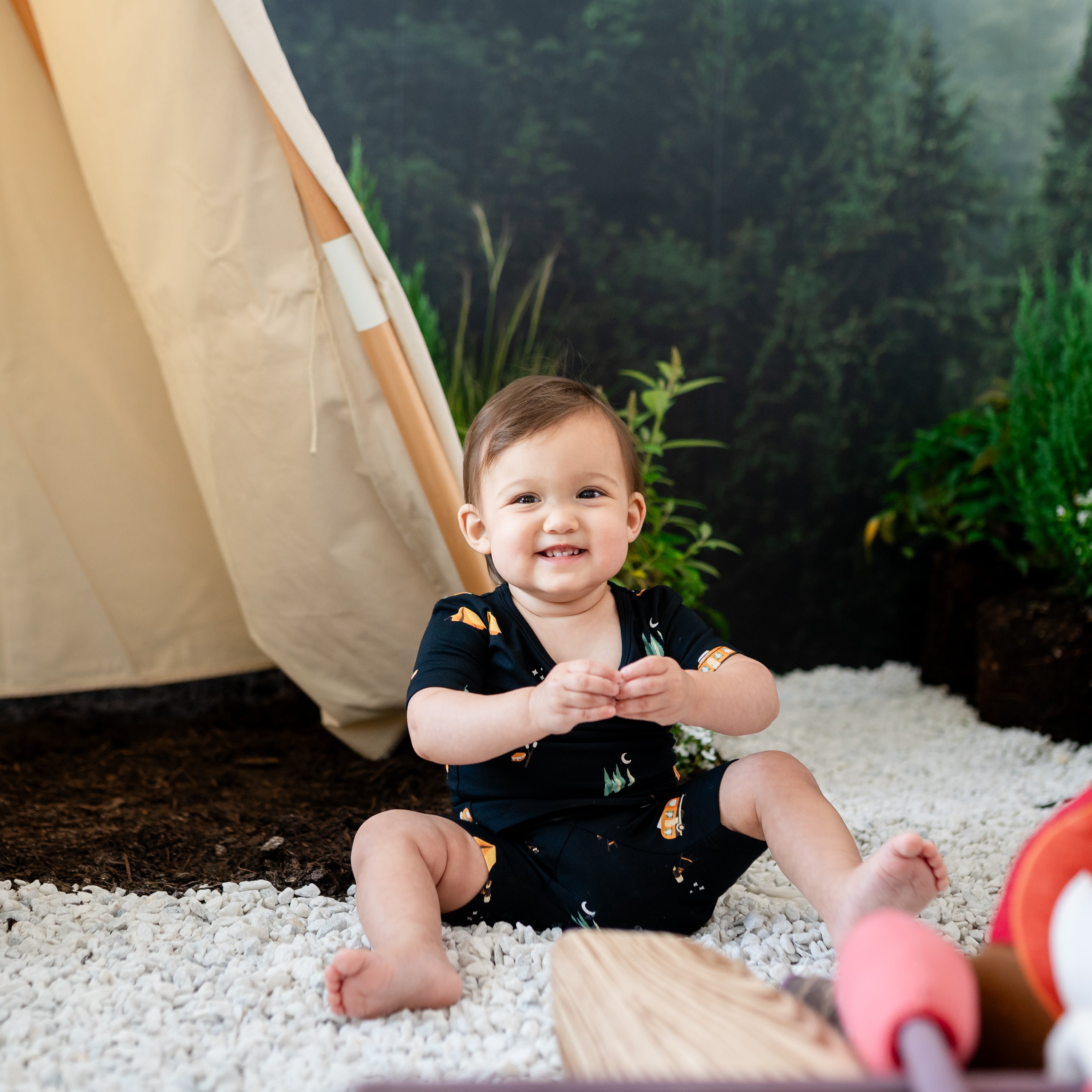 Child sitting in rocks wearing the Short Sleeve Pajamas in Under the Stars with a wilderness camping backdrop