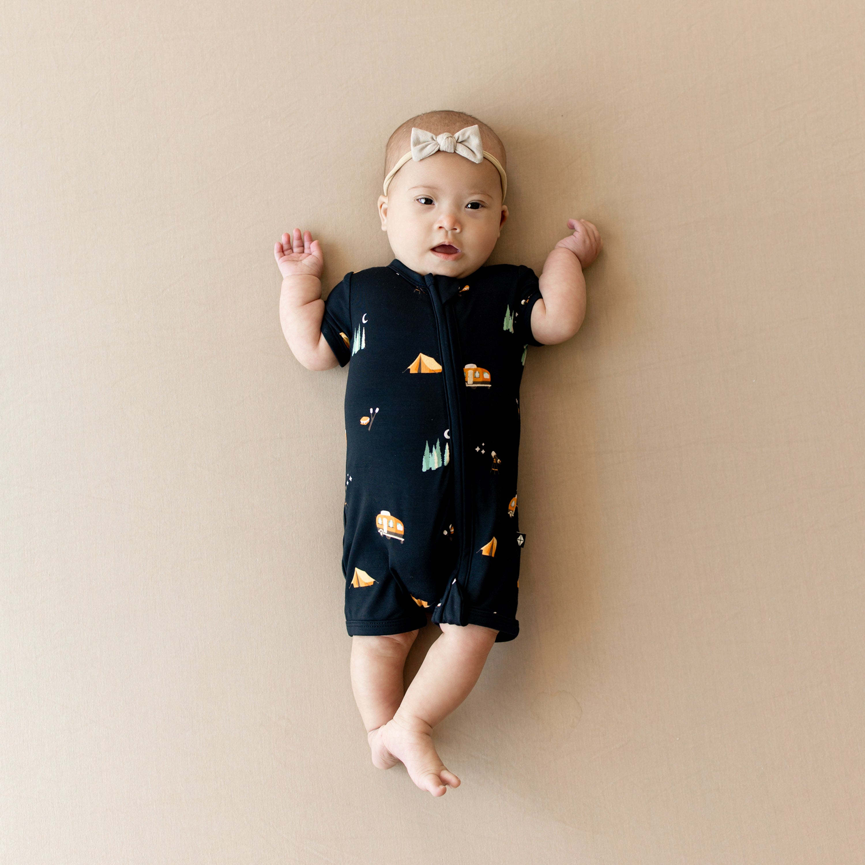 Infant wearing the Zippered Shortall Romper in Under the Stars wearing a tiny nylon bow