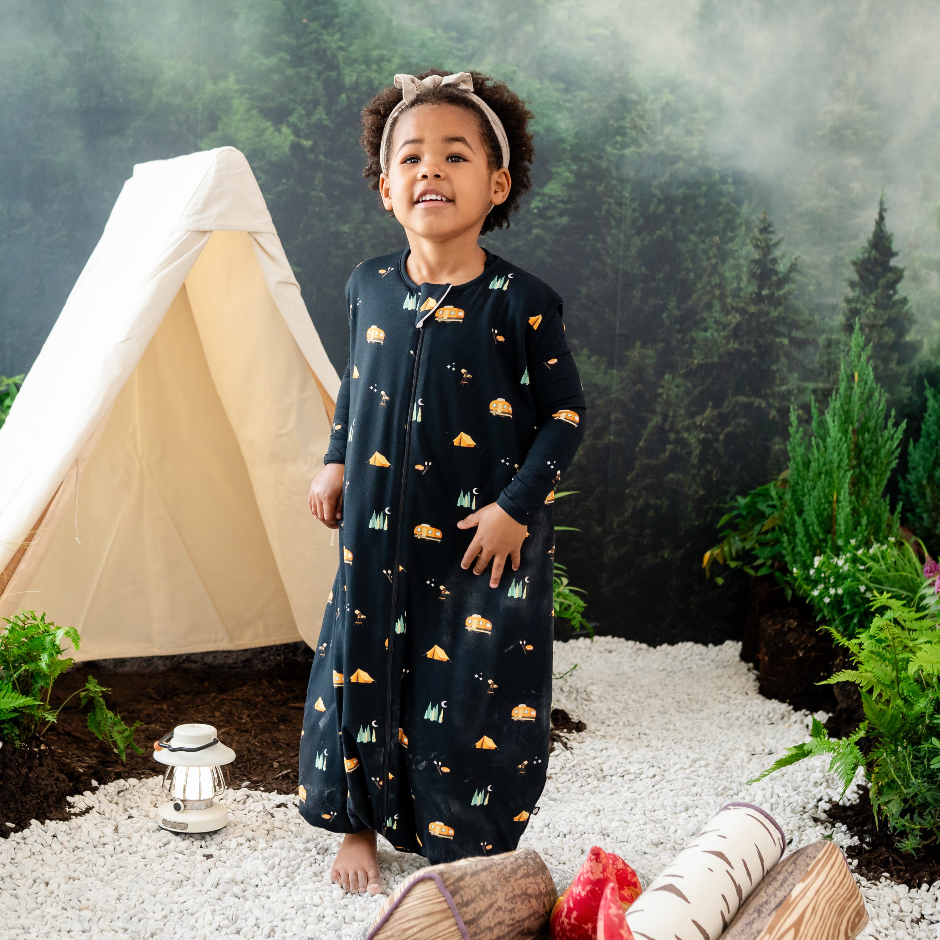 Child model wearing the Sleep Bag Walker in Under the Stars 1.0 standing in rocks in a wilderness inspired camping backdrop