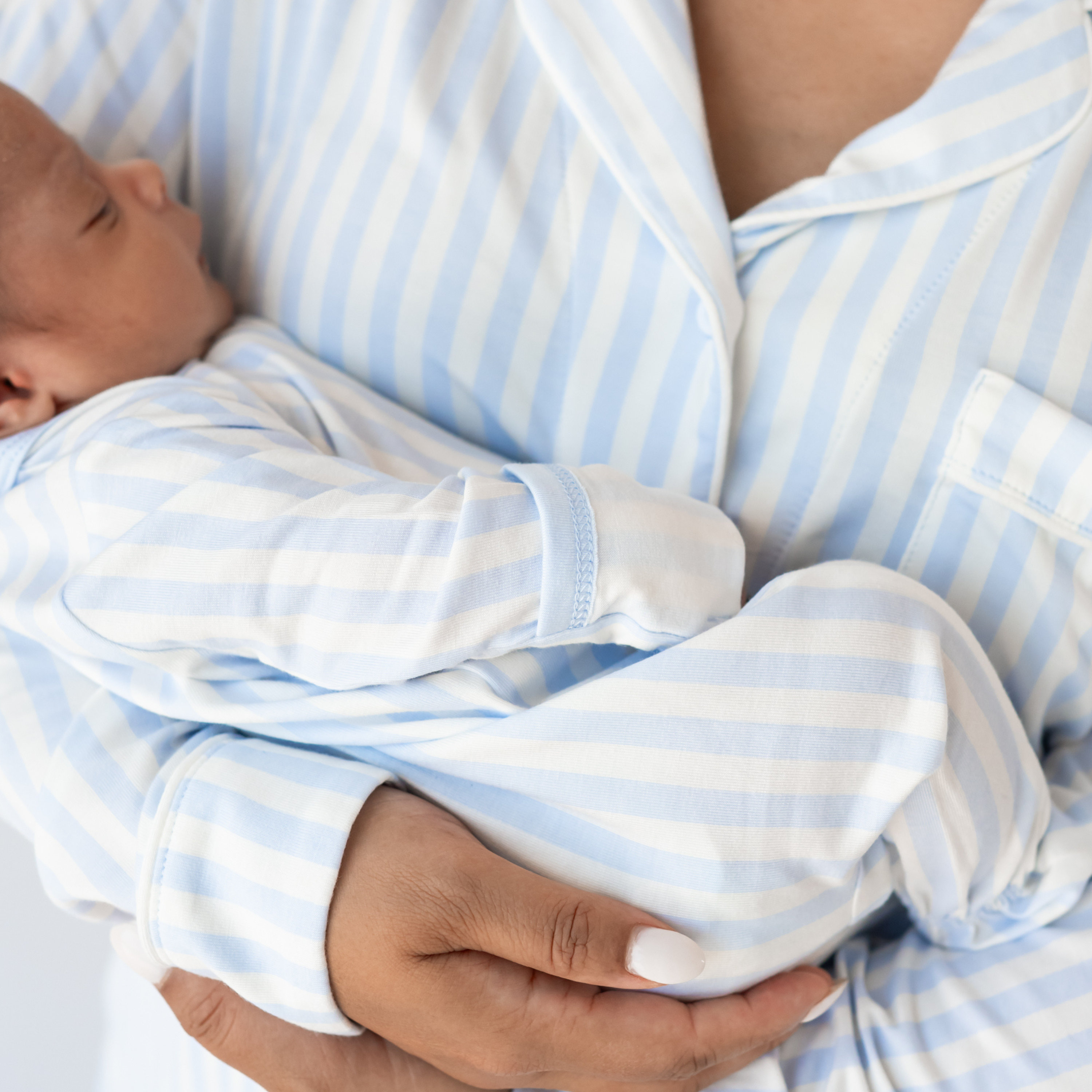 Mom in mist stripe pajama set holding baby in matching footie