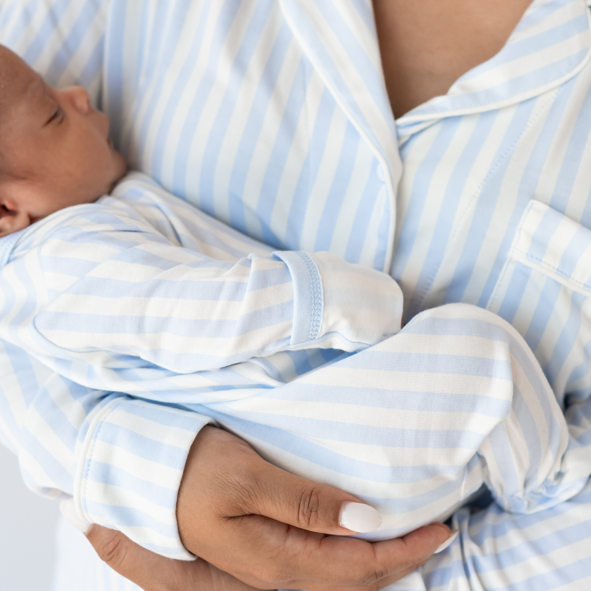 Mom in mist stripe pajama set holding baby in matching footie