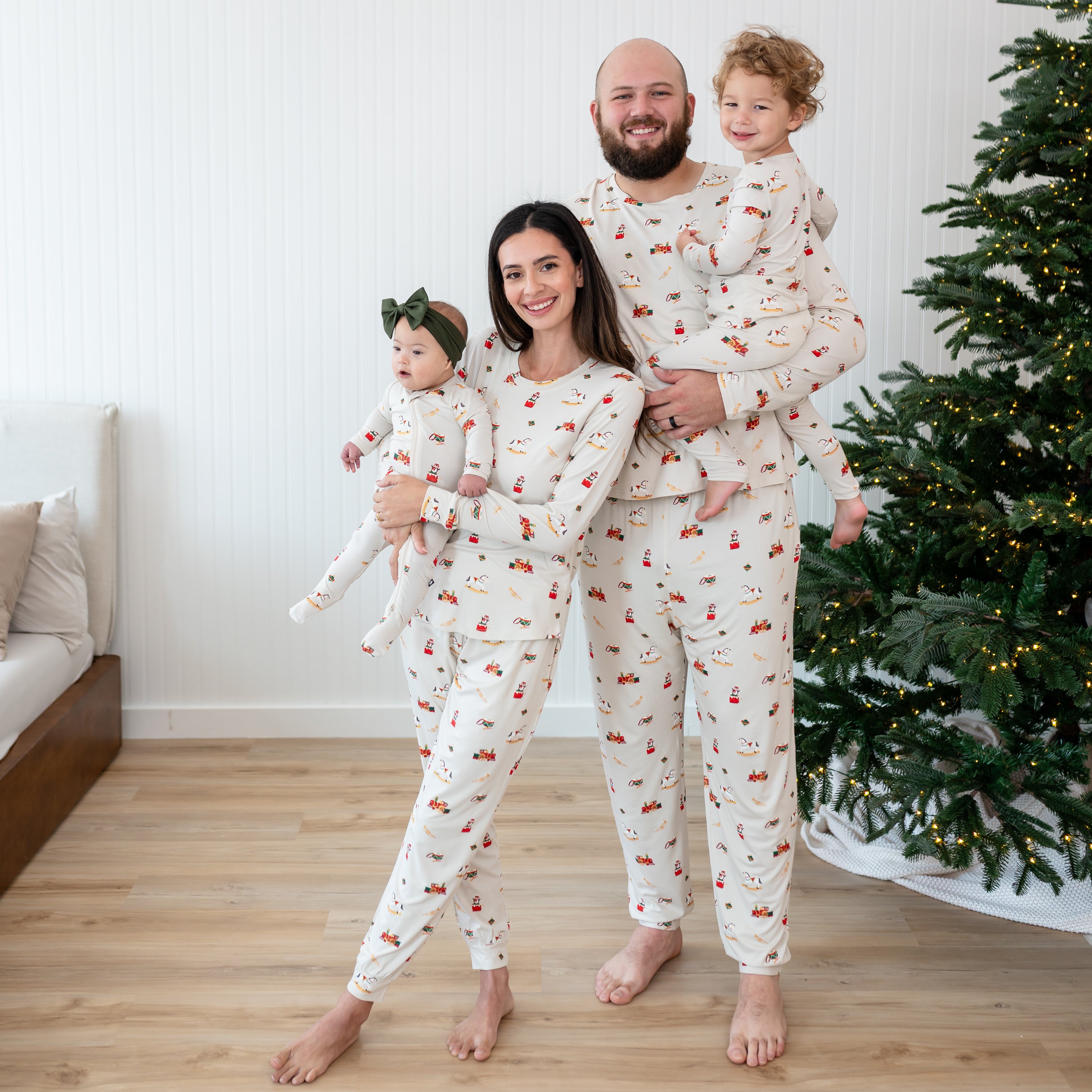 Family of four matching in various Vintage Toys items standing in front of a white paneled wall and lit christmas tree