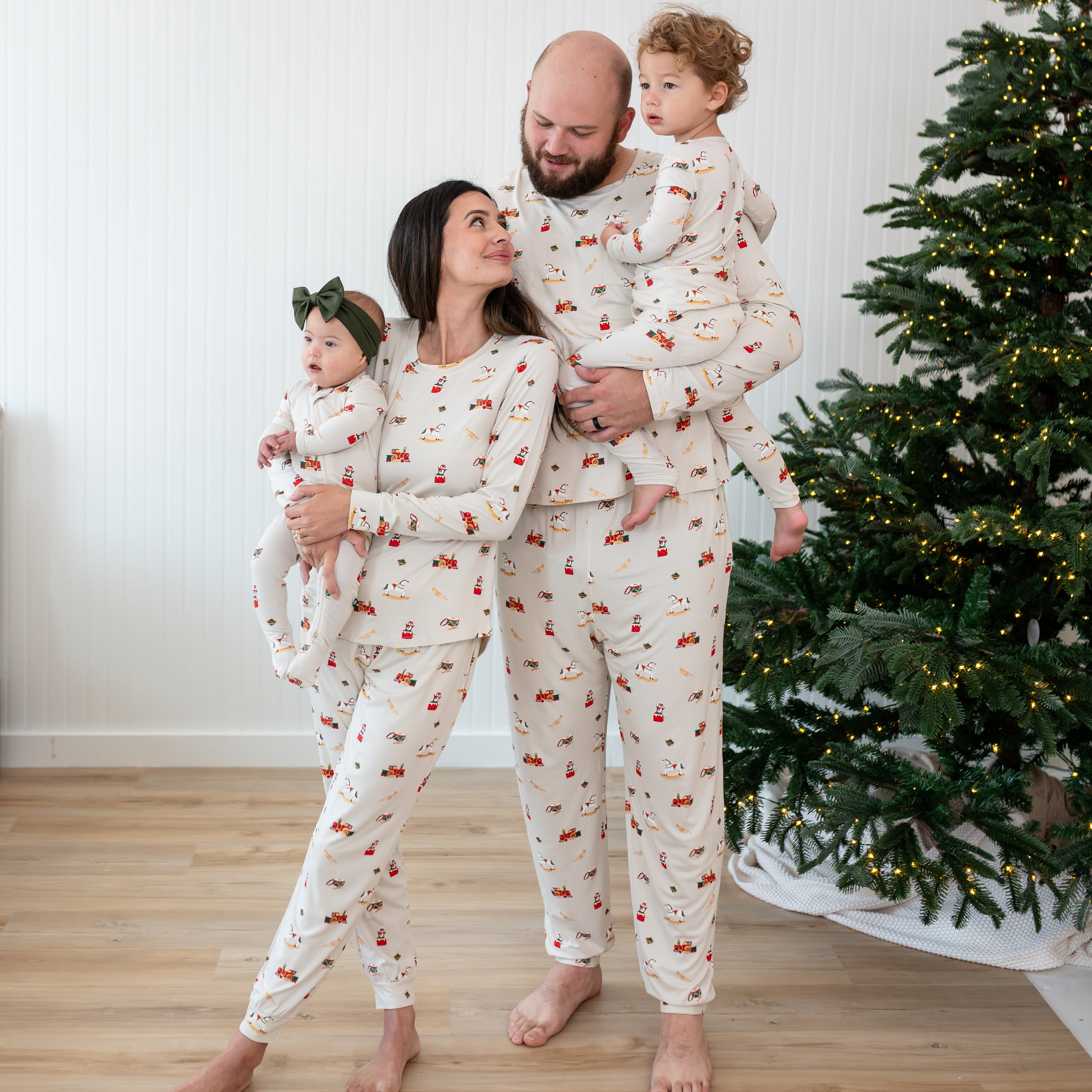 Family of four standing beside a lit Christmas tree matching in Vintage Toys Pajamas