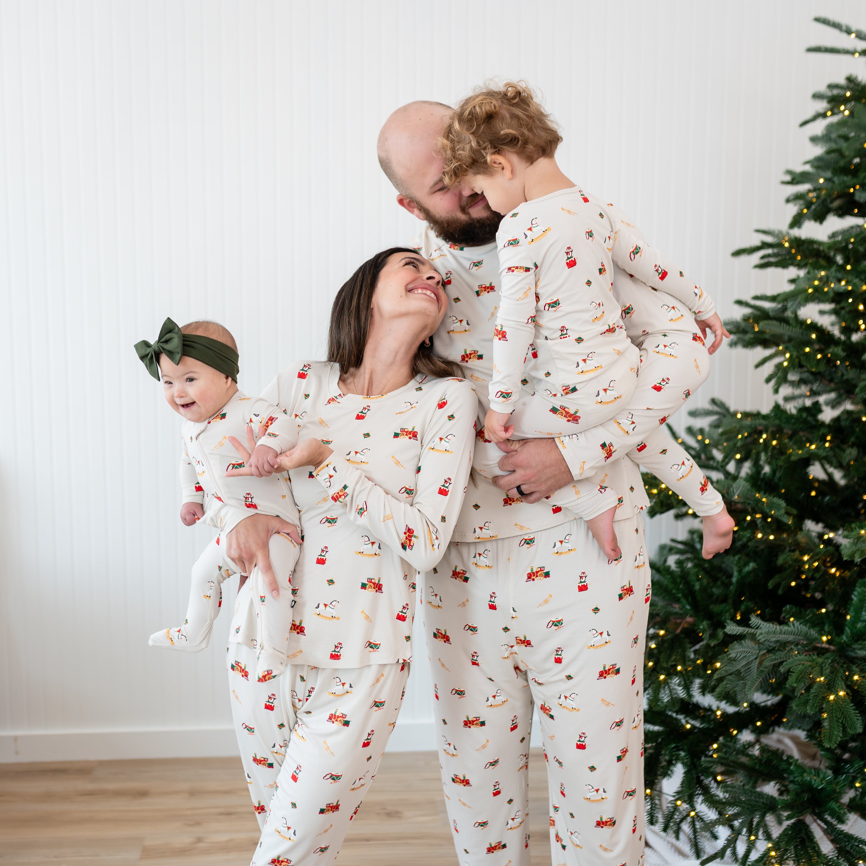 Family of four standing beside a Christmas tree all matching in Vintage Toys pajamas