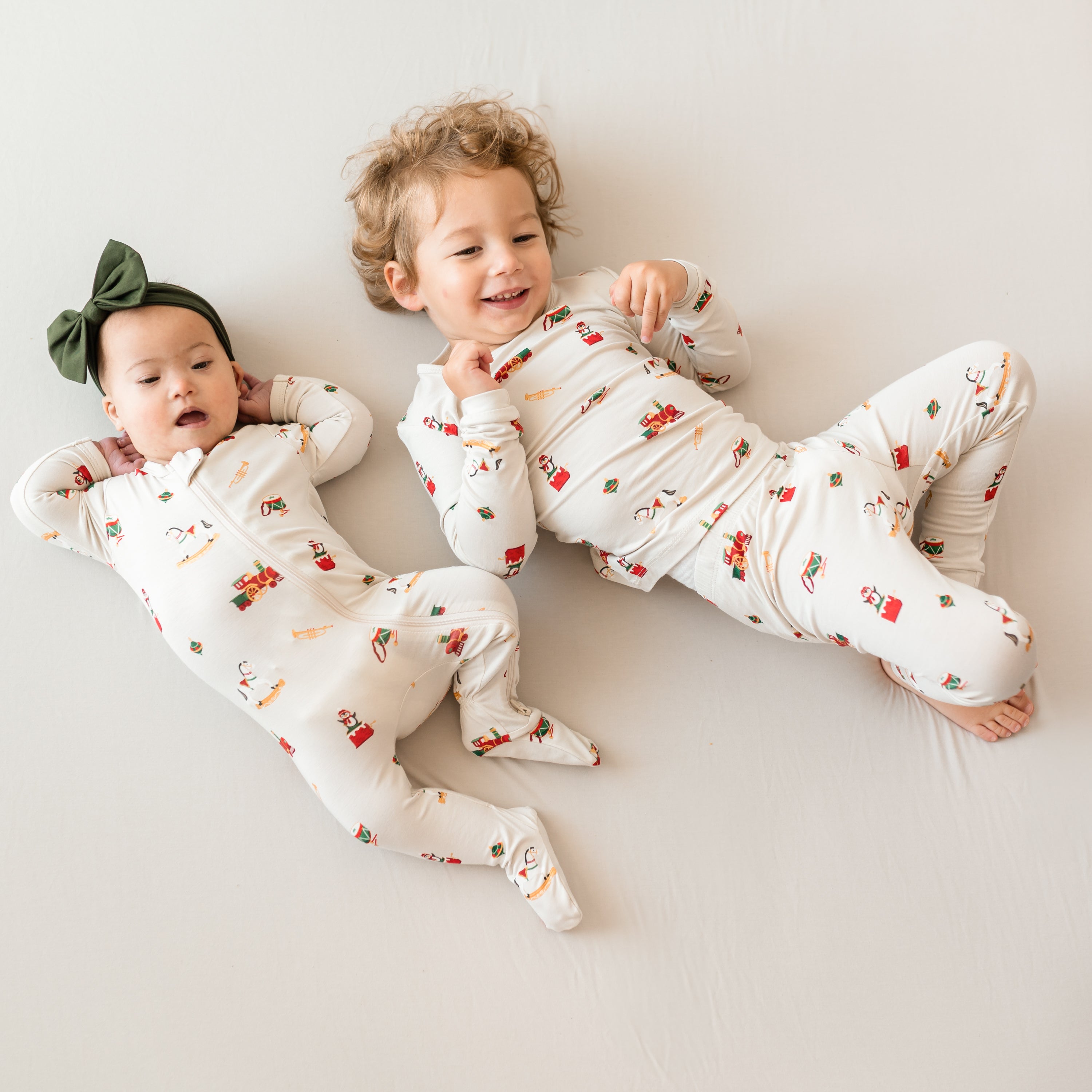 Brother and sister laying side by side on a bed wearing a Zippered Footie in Vintage Toys and long sleeve toddler pajamas in Vintage Toys