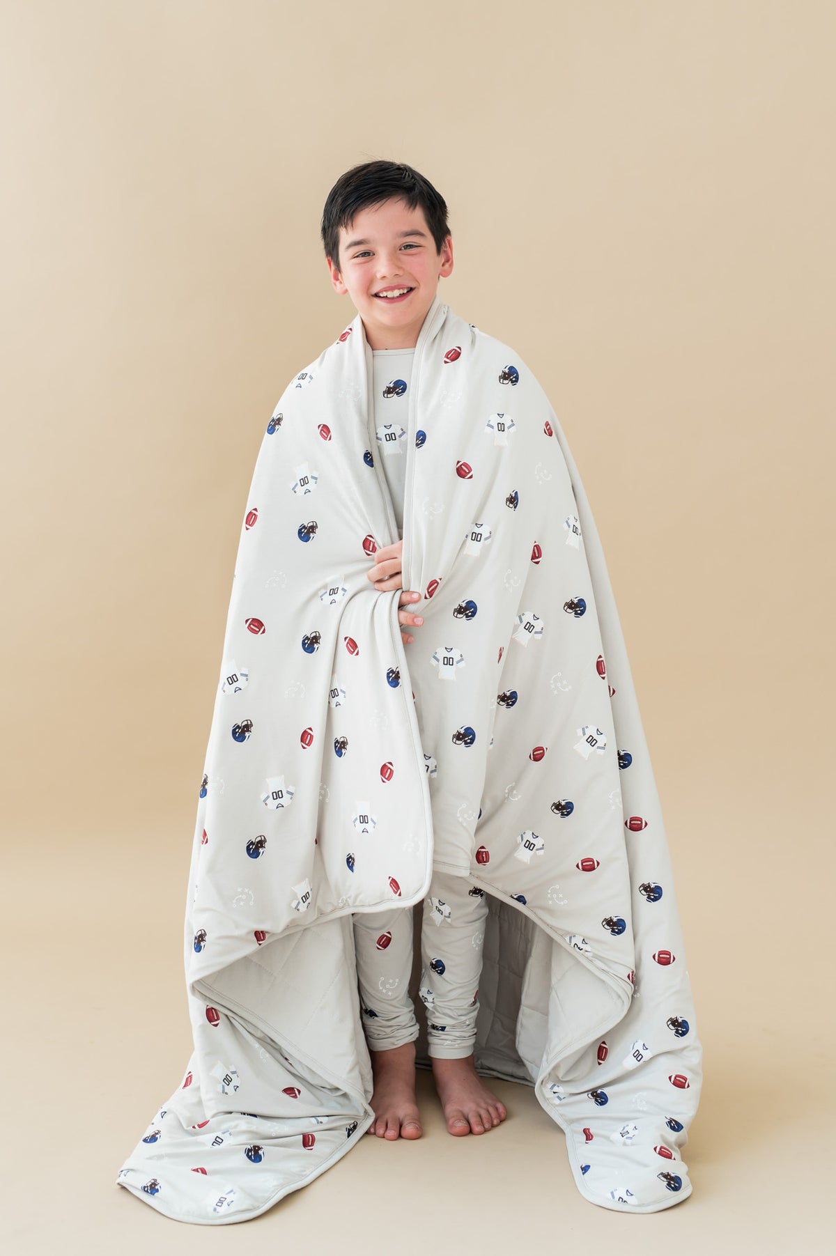 Boy holding Youth Blanket in Vintage Football 2.5 print over his shoulders on a beige background