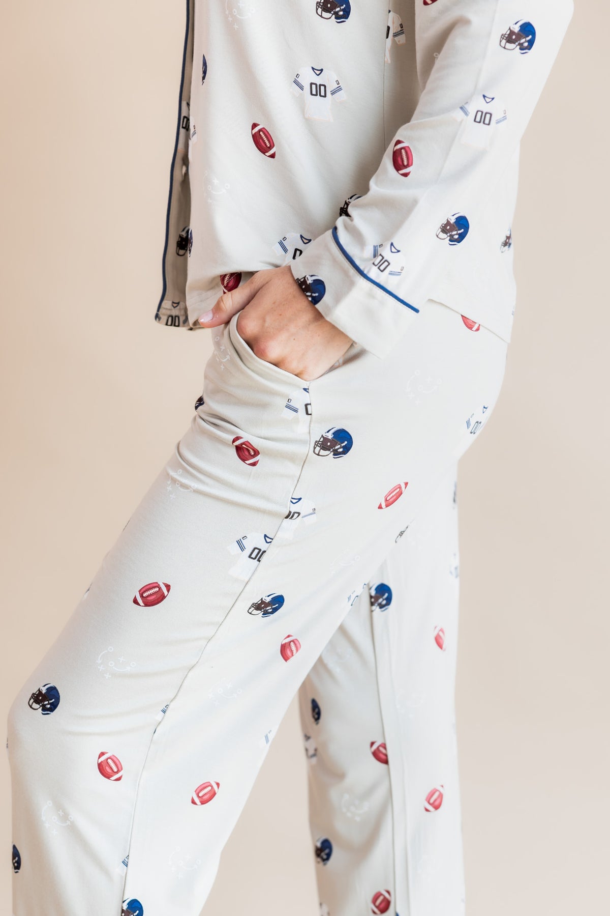 A person wearing a matching cream-colored lounge set with an all-over football and helmet print, featuring a zip-up jacket and wide-leg pants, shown against a solid beige background.
