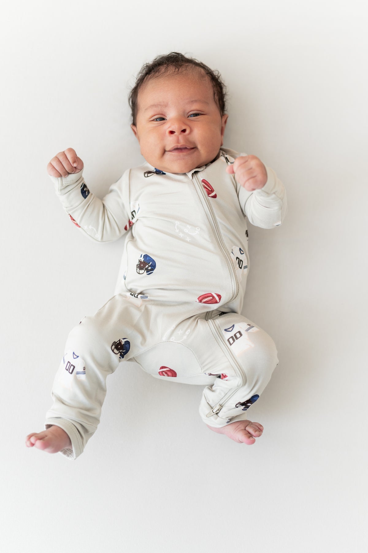 Baby wearing Zippered Romper in Vintage Football print on a cream background