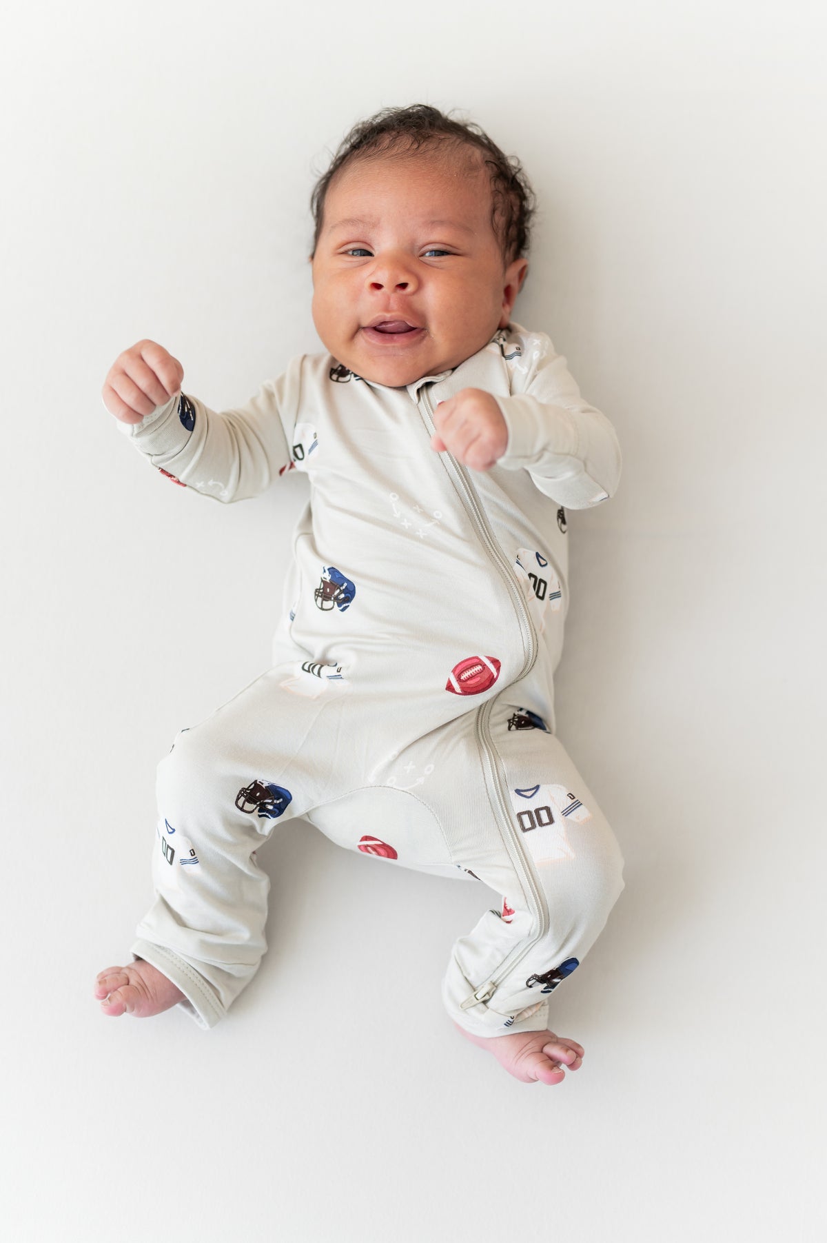 Baby wearing Zippered Romper in Vintage Football print on a cream background