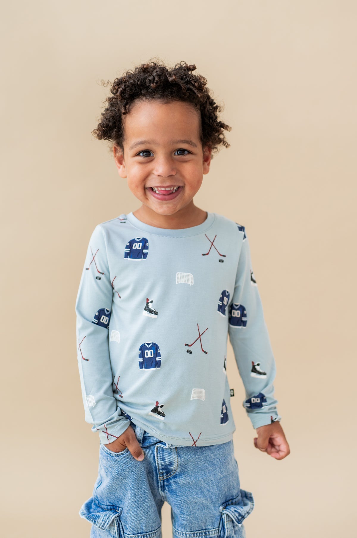 Boy wearing Long Sleeve Toddler Crew Neck Tee in Vintage Hockey print over blue jeans on a beige background