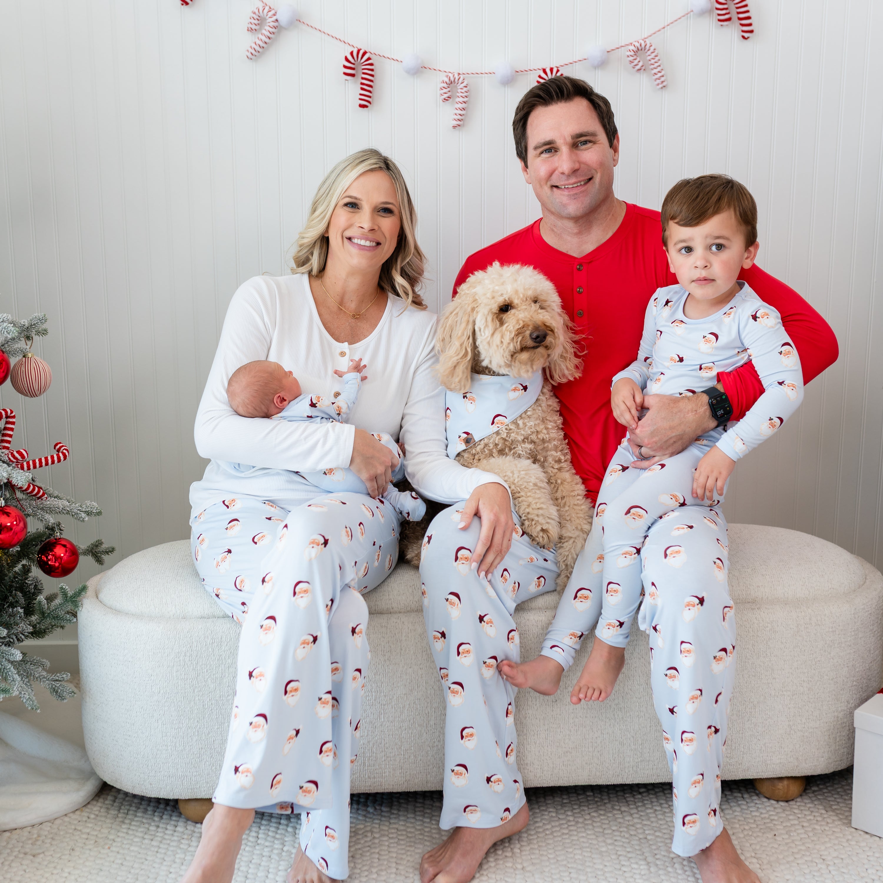 Family of four and a medium sized dog all sitting on a cream colored ottoman matching in various items in Vintage Santa