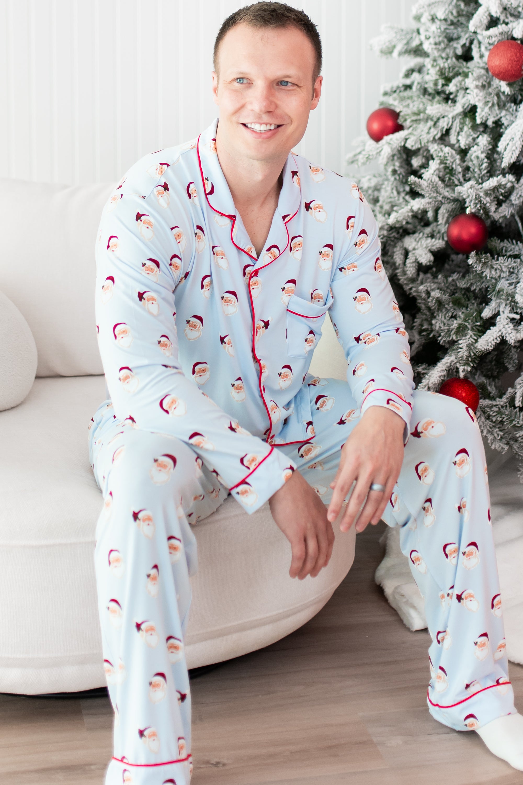 Male model sitting on a cream sofa wearing the Men's Long Sleeve Pajama Set in Vintage Santa
