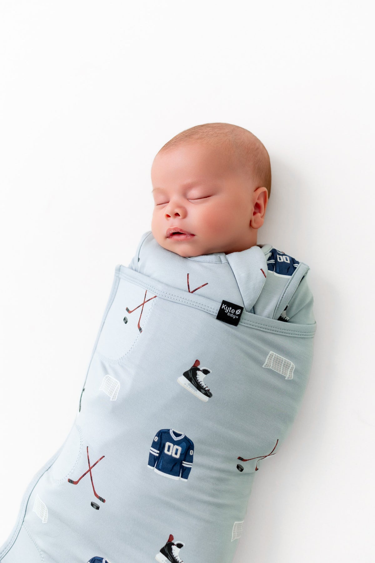 Baby sleeping in Sleep Bag Swaddler with Vintage Hockey 1.0 print on a white background
