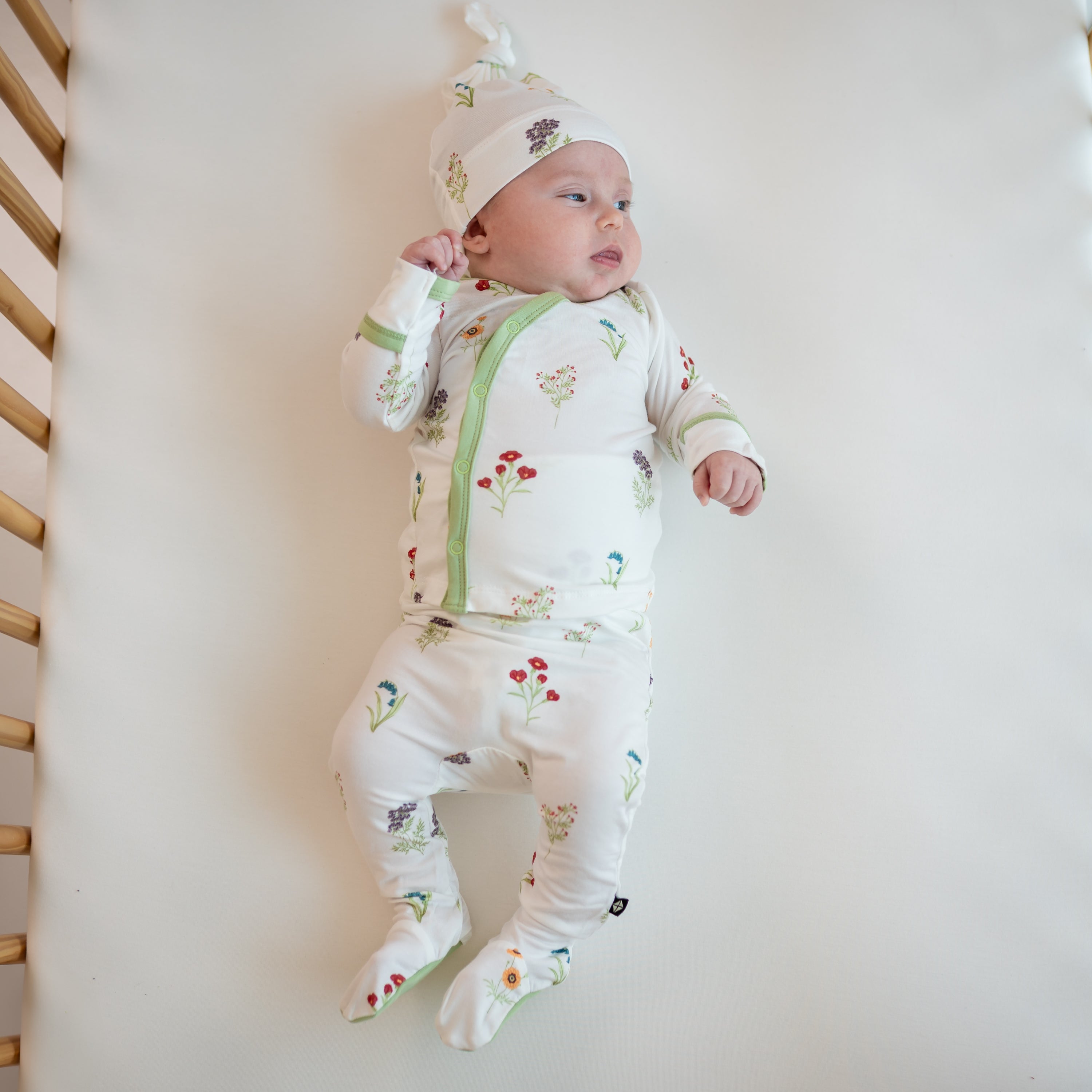 Baby wearing Take Me Home Set with Cap in Wildflower in a crib
