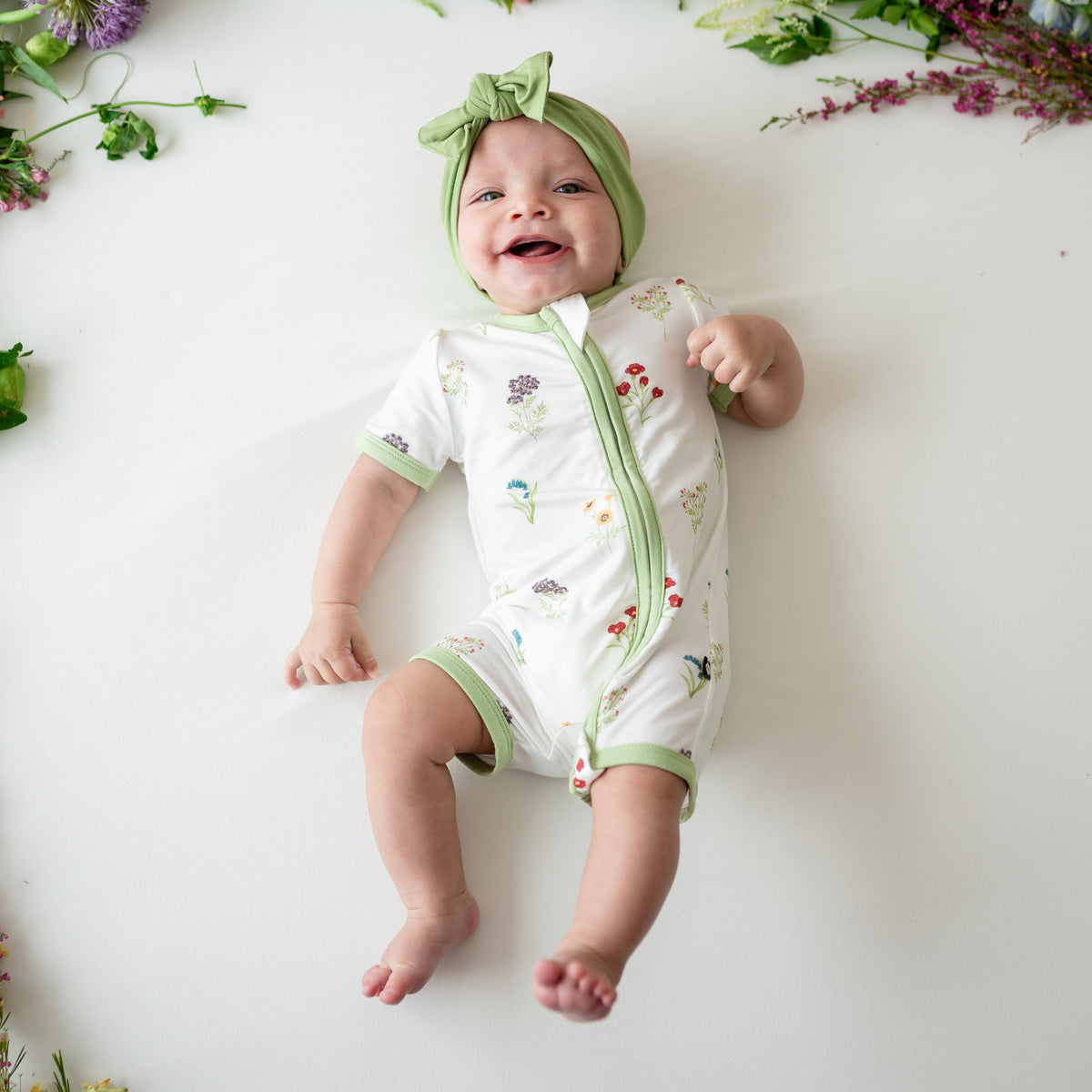 Baby smiling wearing Zippered Shortall Romper in Wildflower and Honu bow