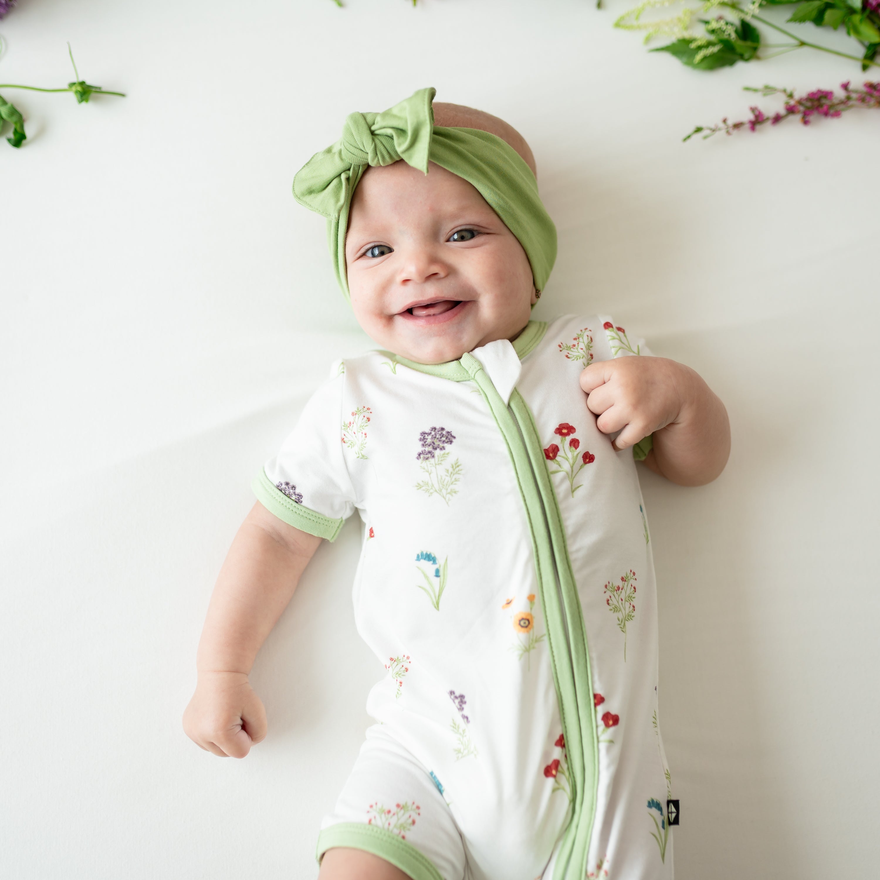 Close up of Baby smiling wearing Zippered Shortall Romper in Wildflower and Honu bow
