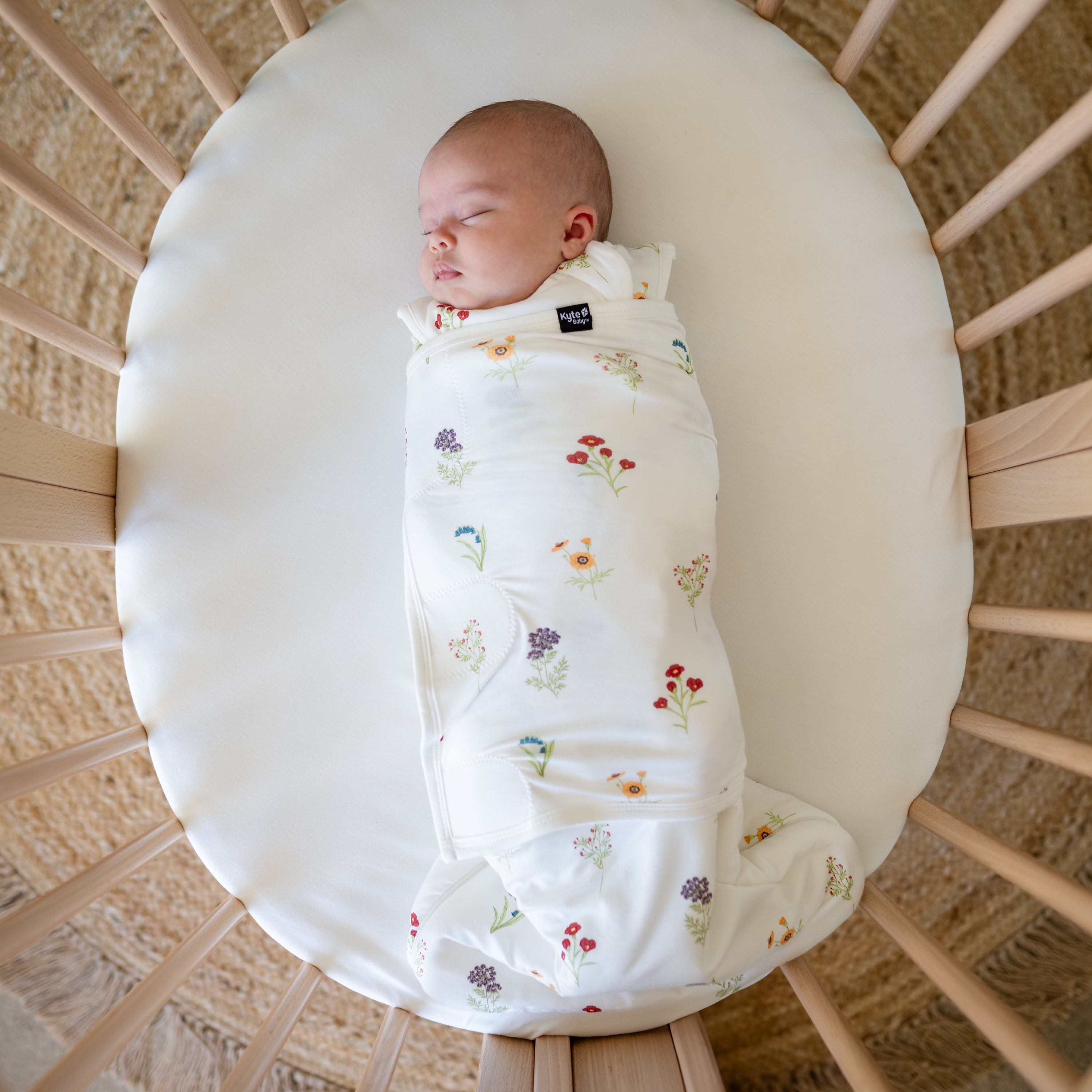Baby sleeping in a oval bassinet wearing Sleep Bag Swaddler in Wildflower 1.0