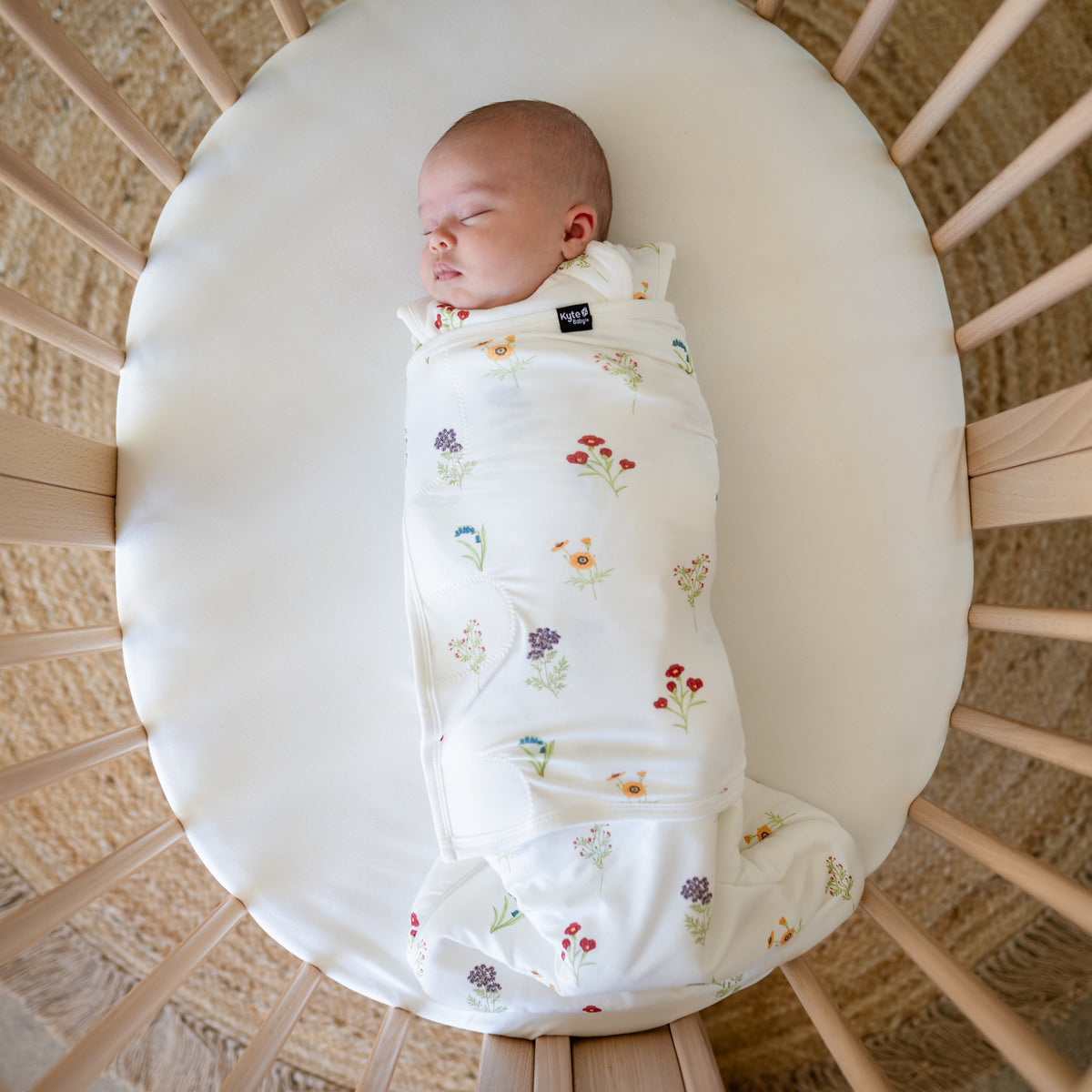 Baby sleeping in a oval bassinet wearing Sleep Bag Swaddler in Wildflower 1.0