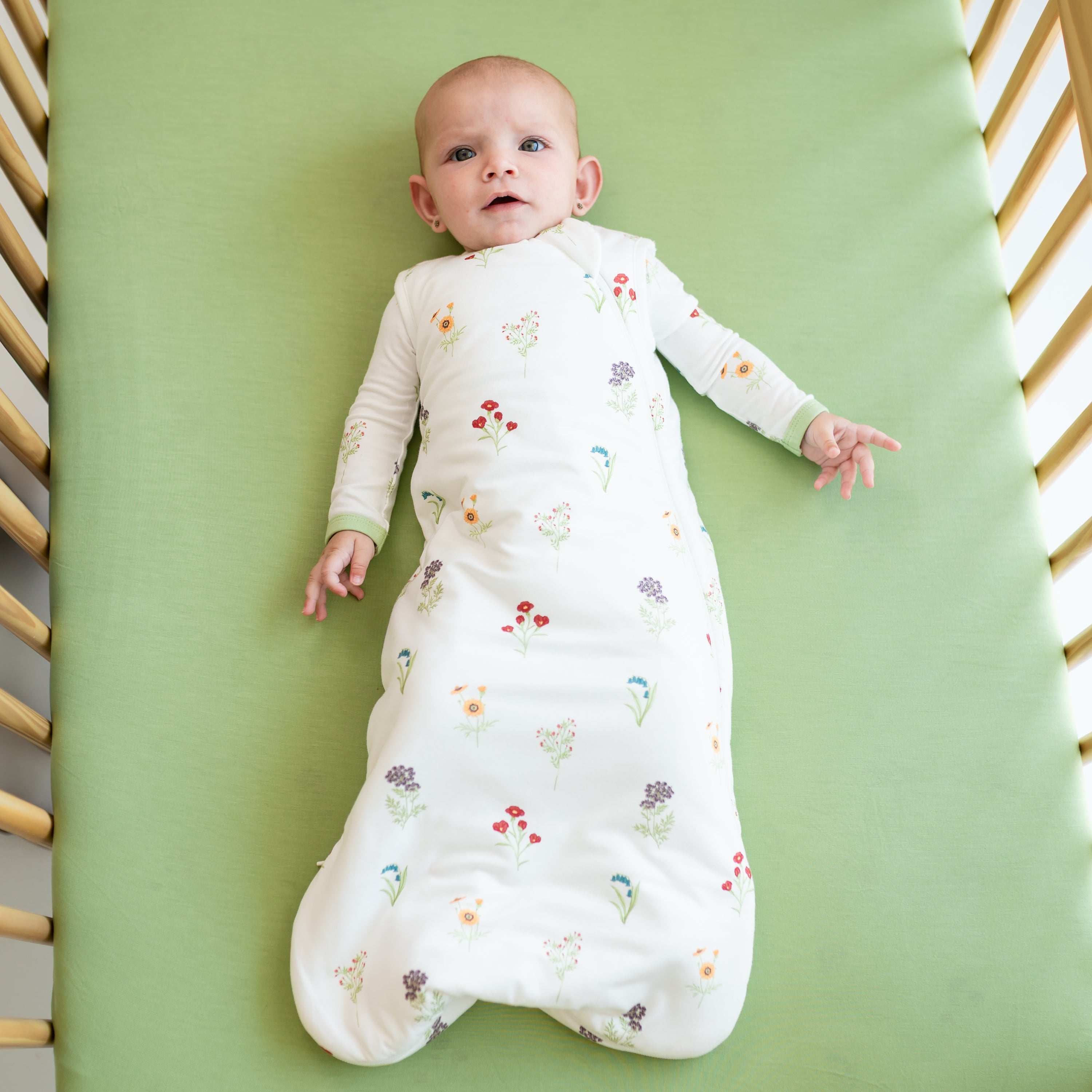 Baby wearing Sleep Bag in Wildflower 1.0 on a honu crib sheet