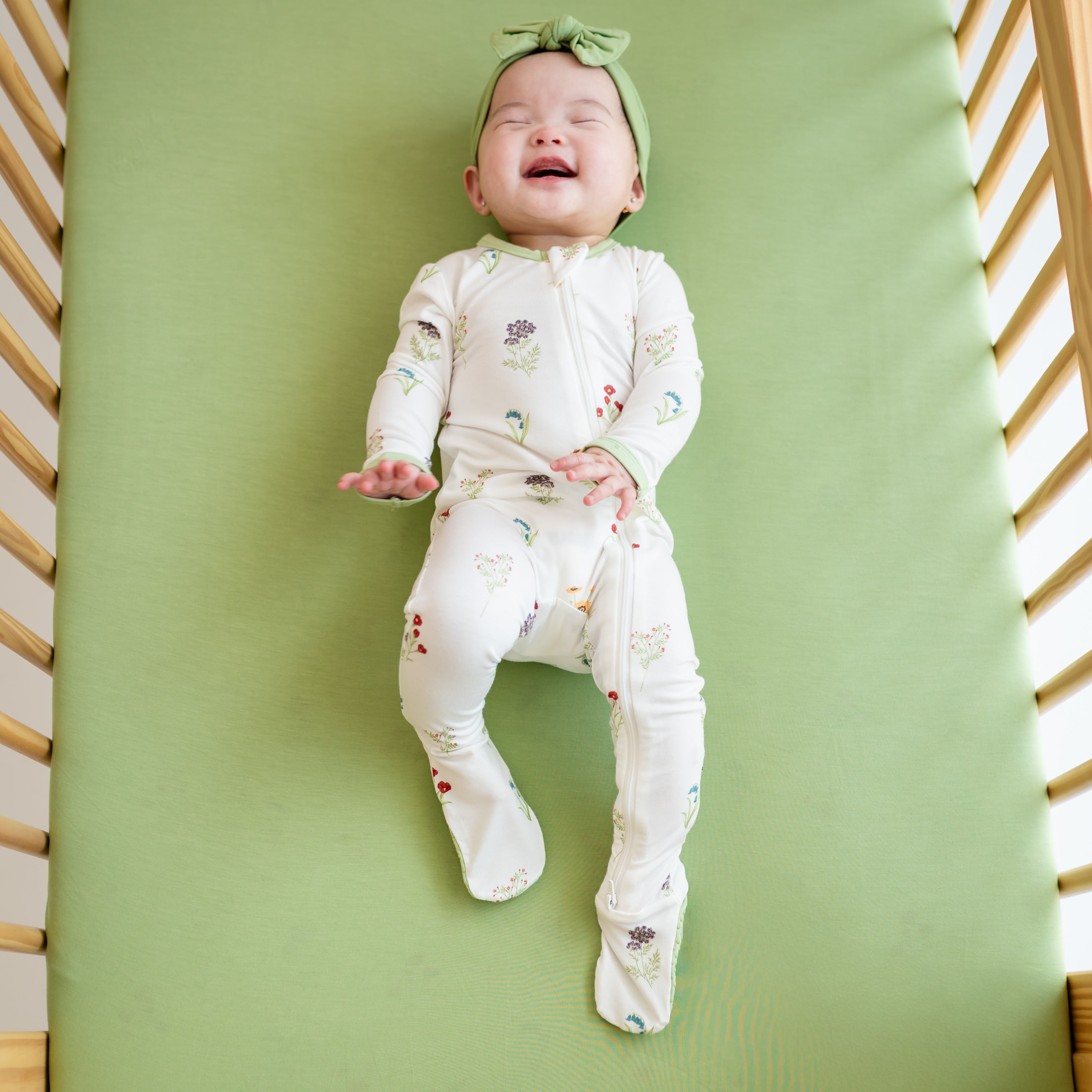 Baby smiling wearing Zippered Footie in Wildflower in a crib