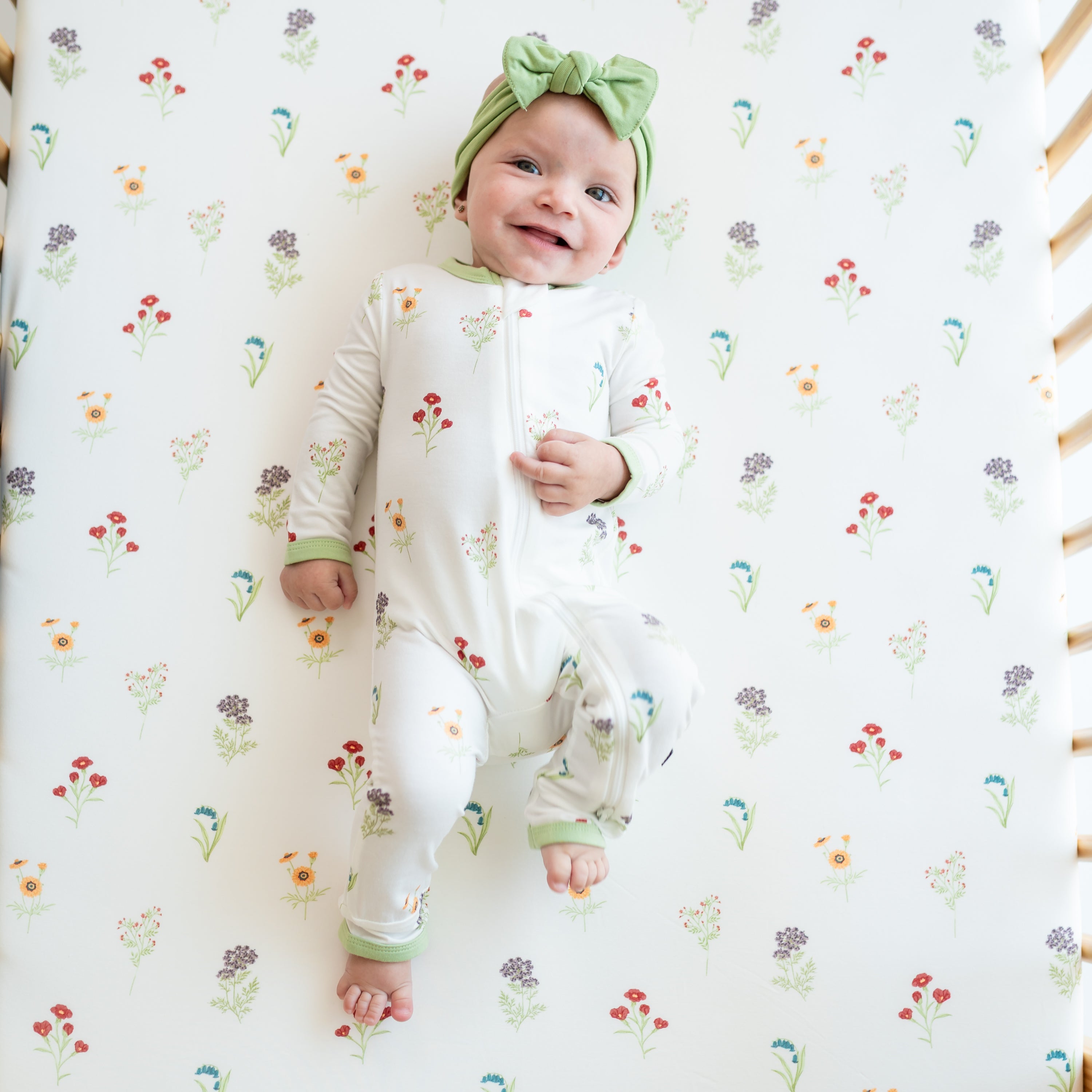 Baby wearing Zippered Romper in Wildflower in a crib with Crib Sheet in Wildflower on