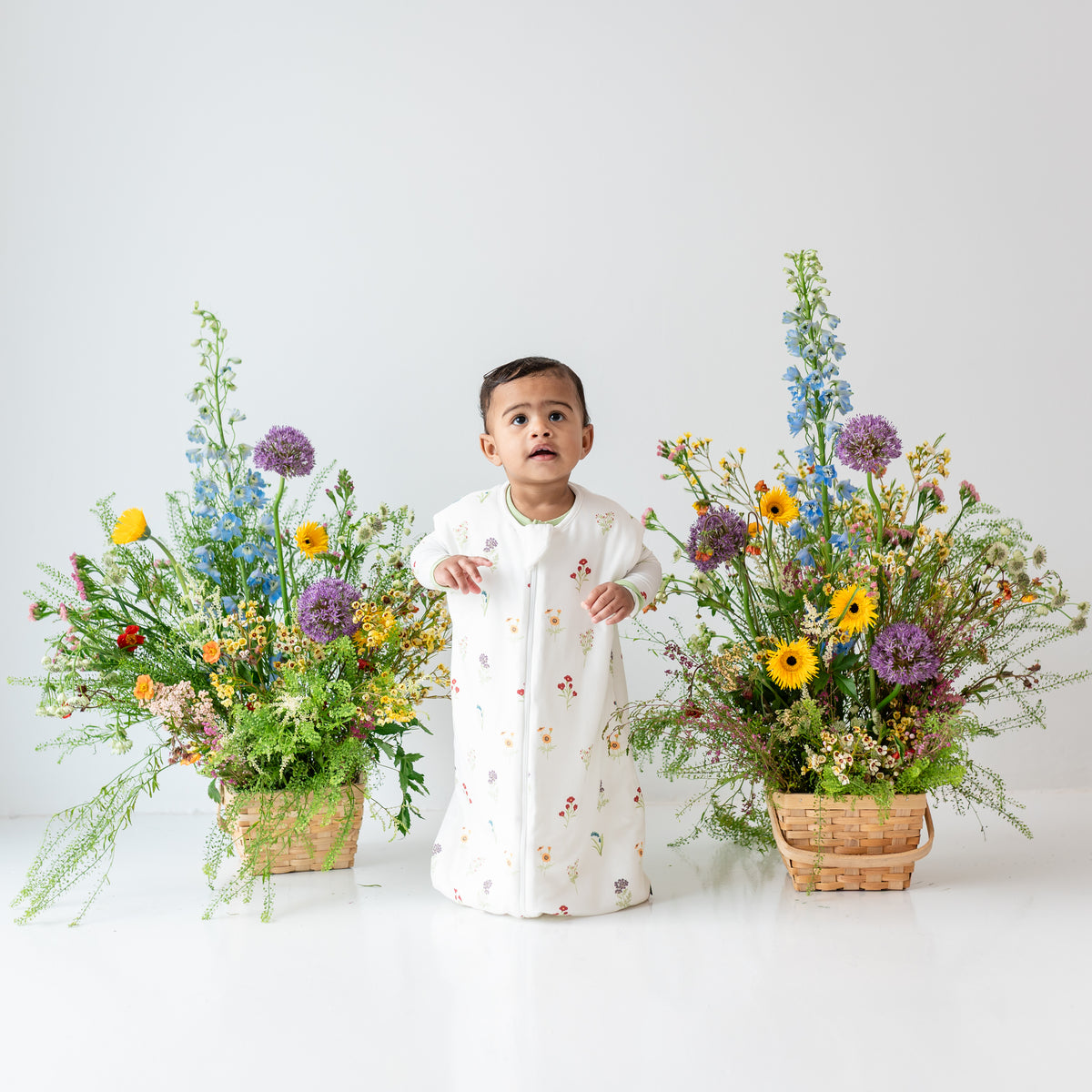 Toddler wearing Sleep Bag Walker in Wildflower 1.0 next to flowers