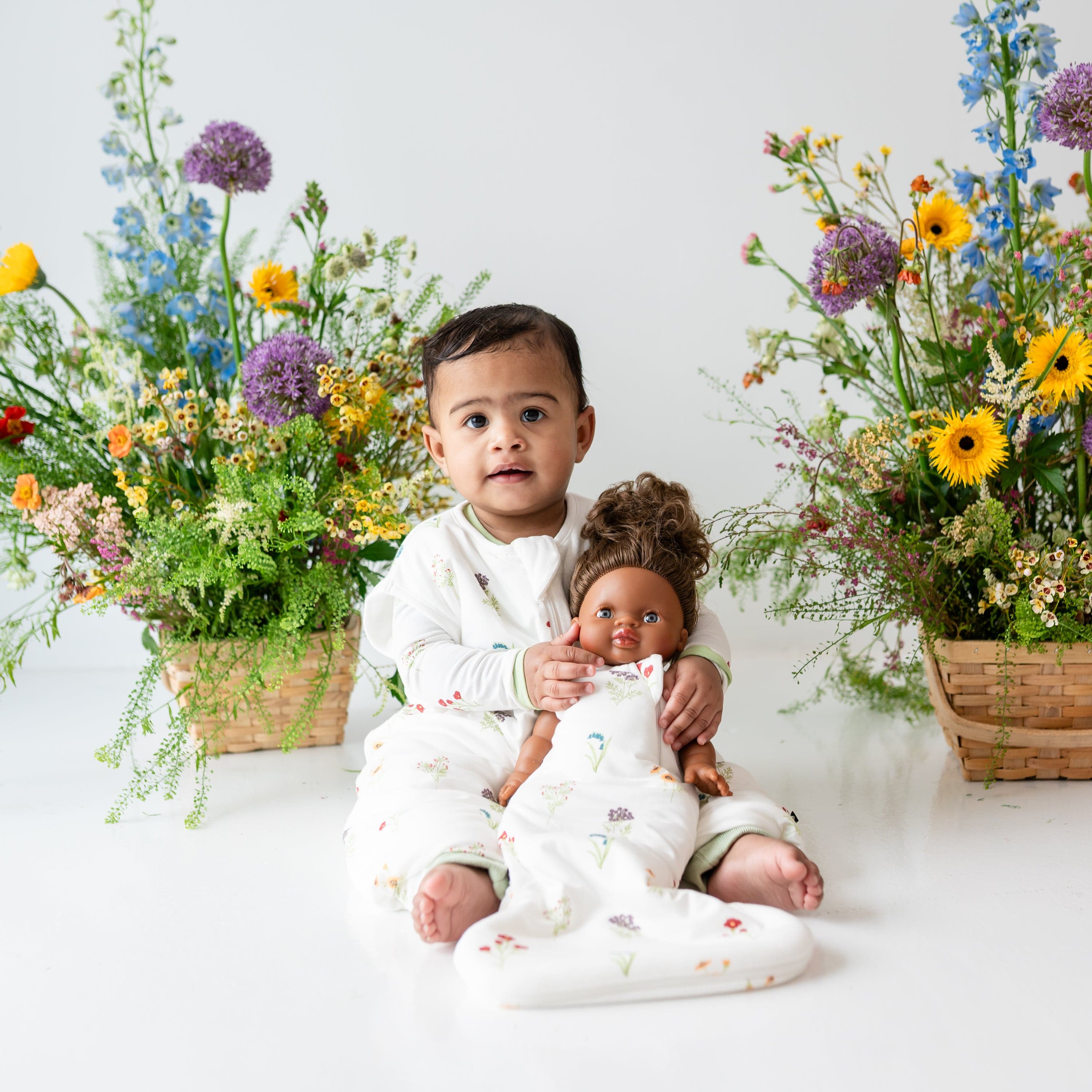 Toddler wearing Sleep Bag Walker in Wildflower 1.0 holding a baby doll with Wildflower Baby Doll Sleep Bag