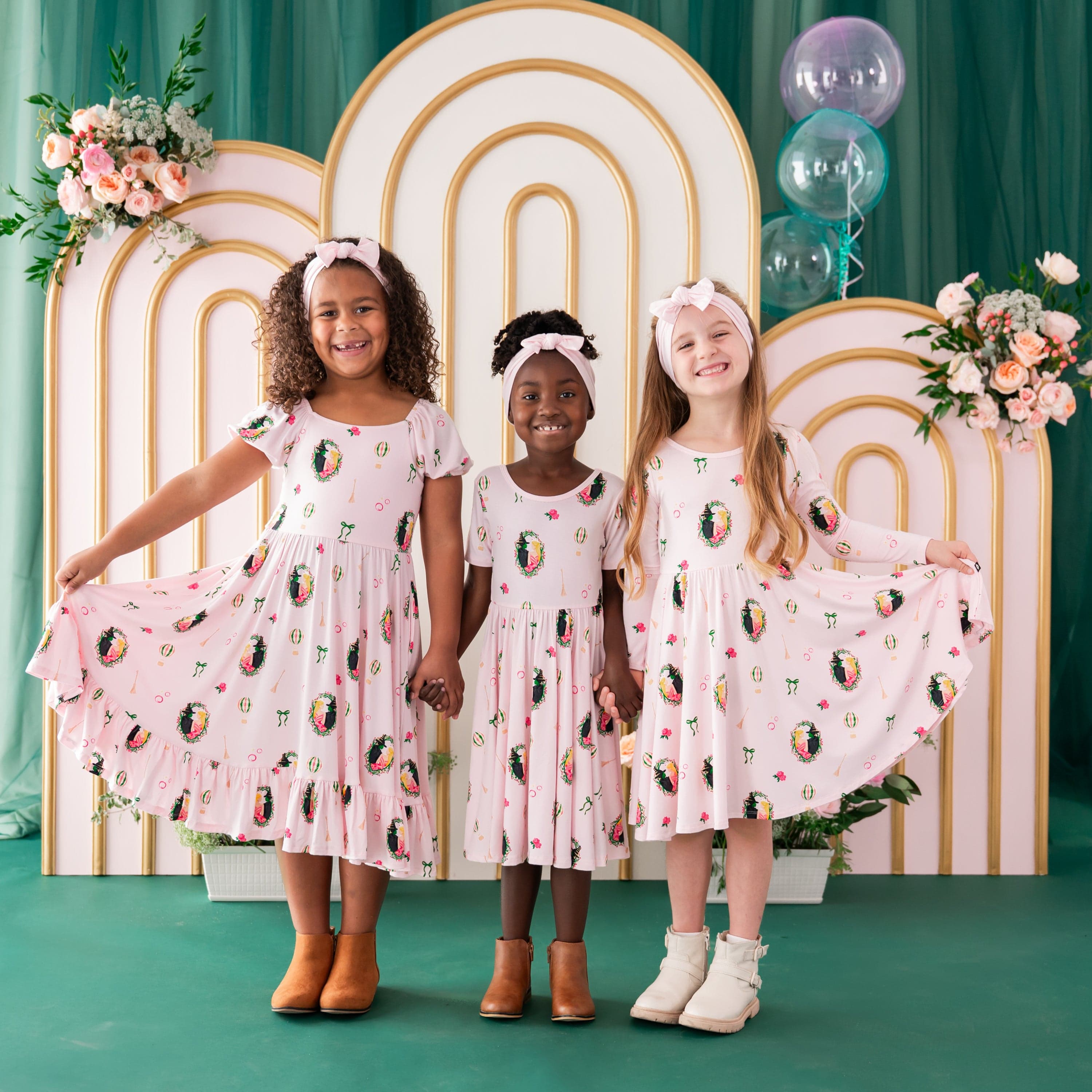 Three girls standing side by side holding hands wearing the puff sleeve, short sleeve and long sleeve twirl dress in Wicked