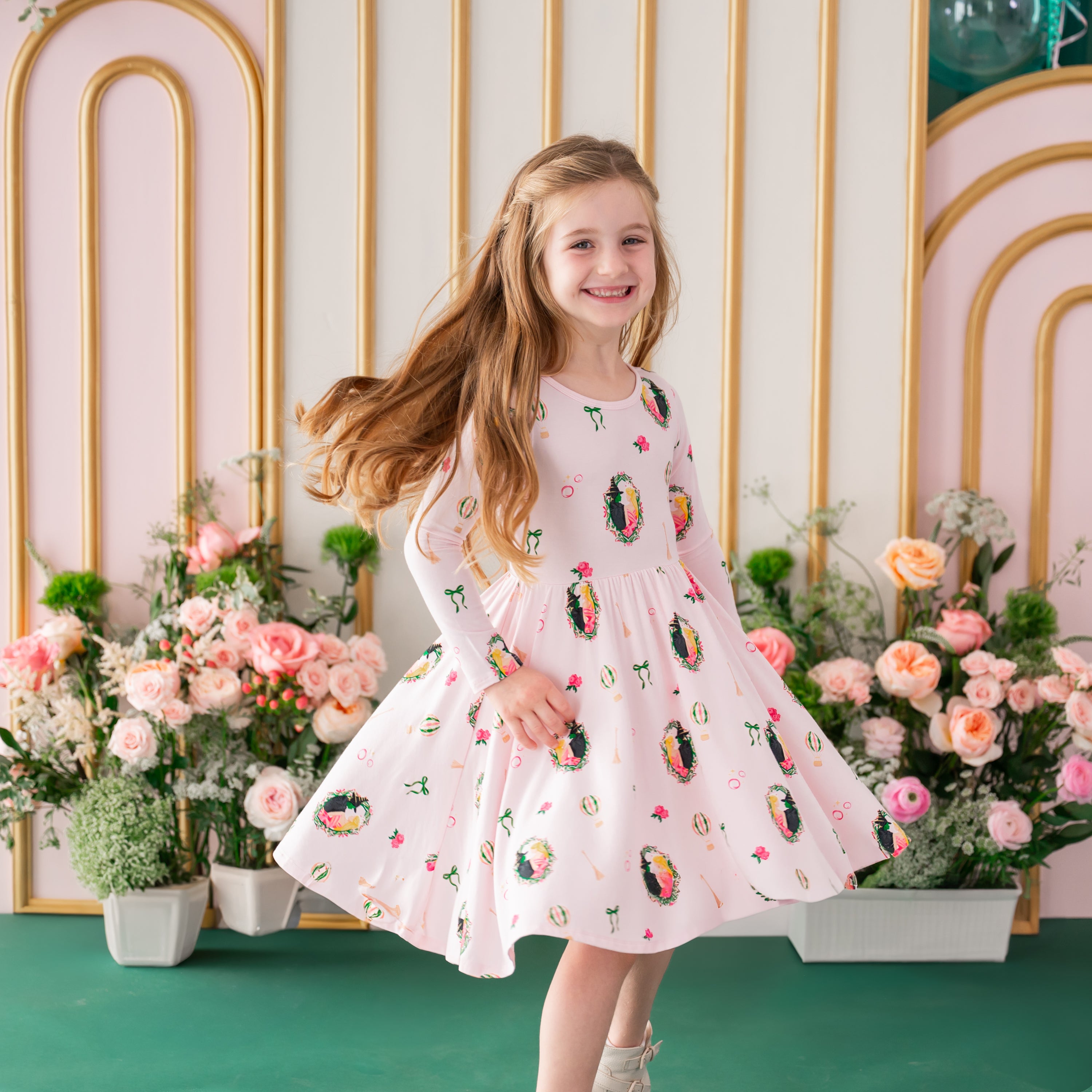Young girl twirling in the Long Sleeve Twirl Dress in Wicked in front of a floral backdrop