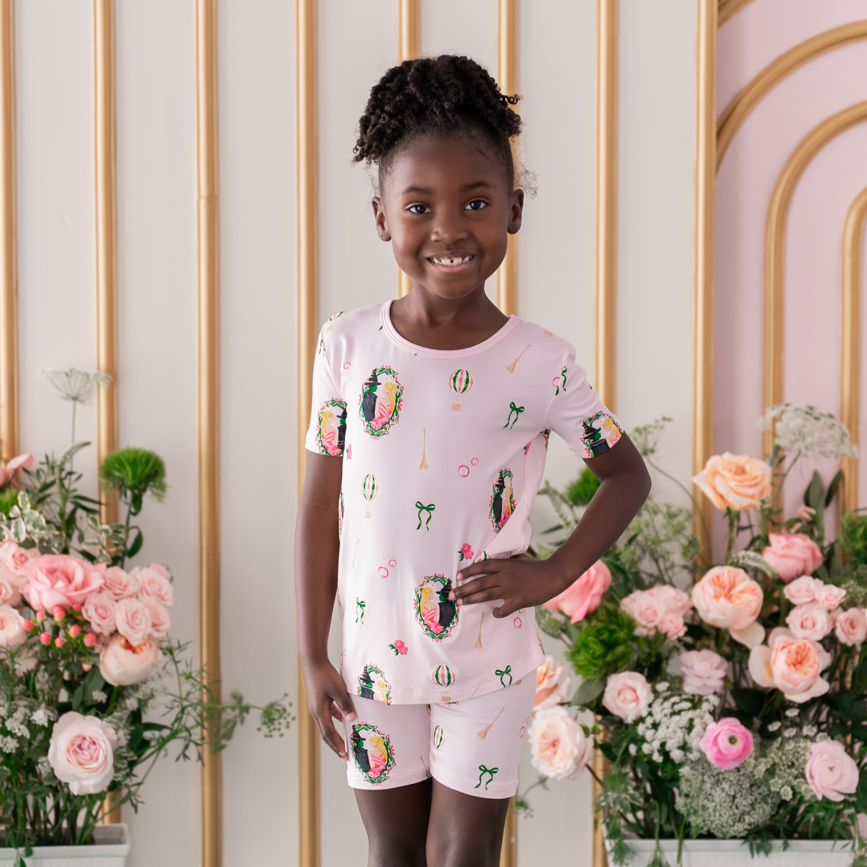 Smiling girl standing with one hand on her hip wearing the Short Sleeve Pajamas in Wicked in front of a flower backdrop