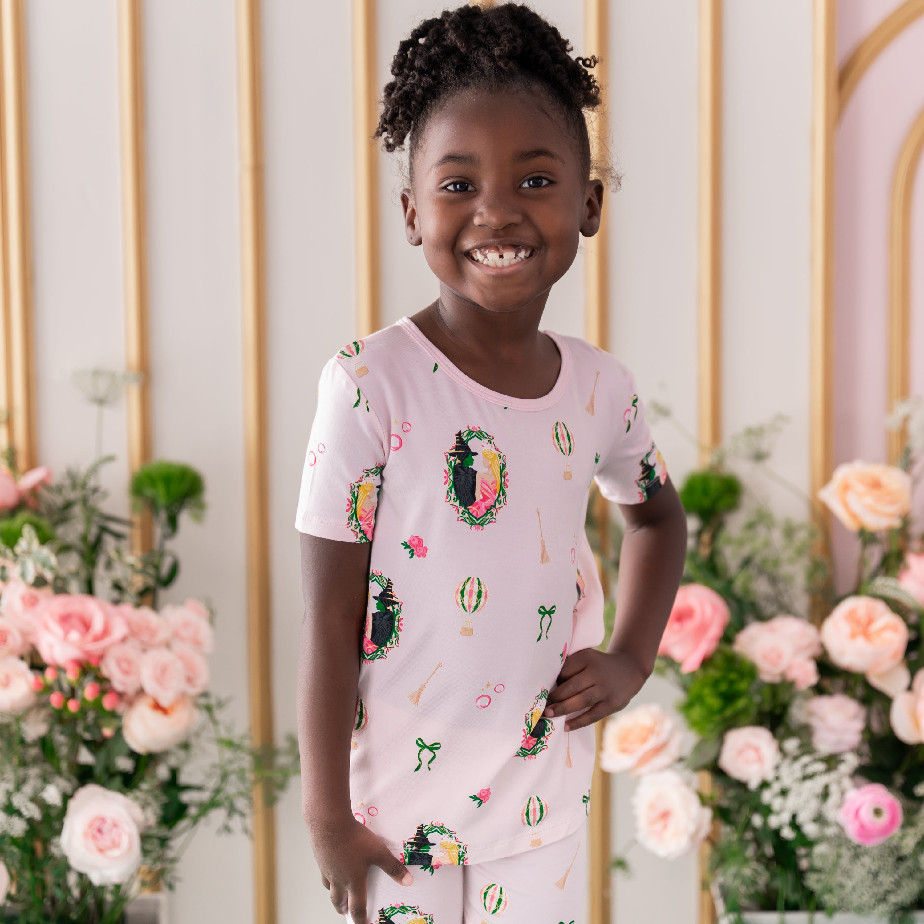 Close up of young girl wearing the Short Sleeve Pajamas in Wicked standing with one hand on her hip in front of a flower backdrop