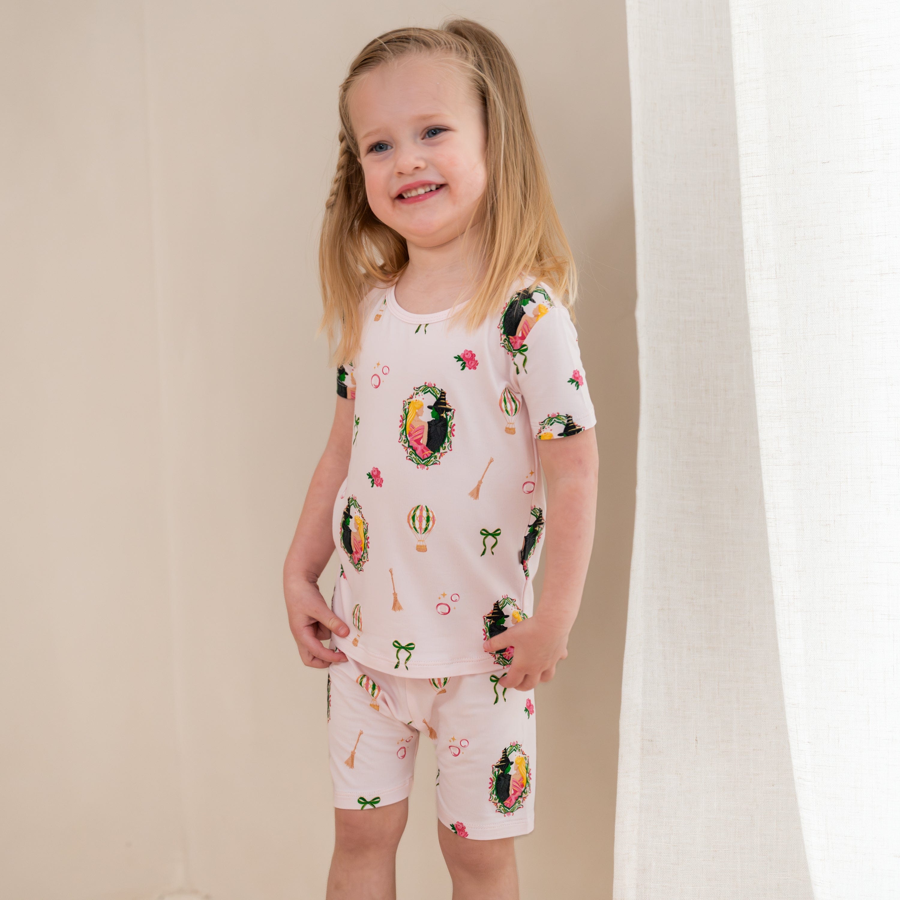 Young smiling girl standing in front of a light beige wall wearing the Short Sleeve Pajamas in Wicked