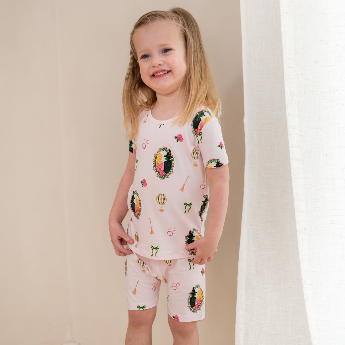 Young smiling girl standing in front of a light beige wall wearing the Short Sleeve Pajamas in Wicked