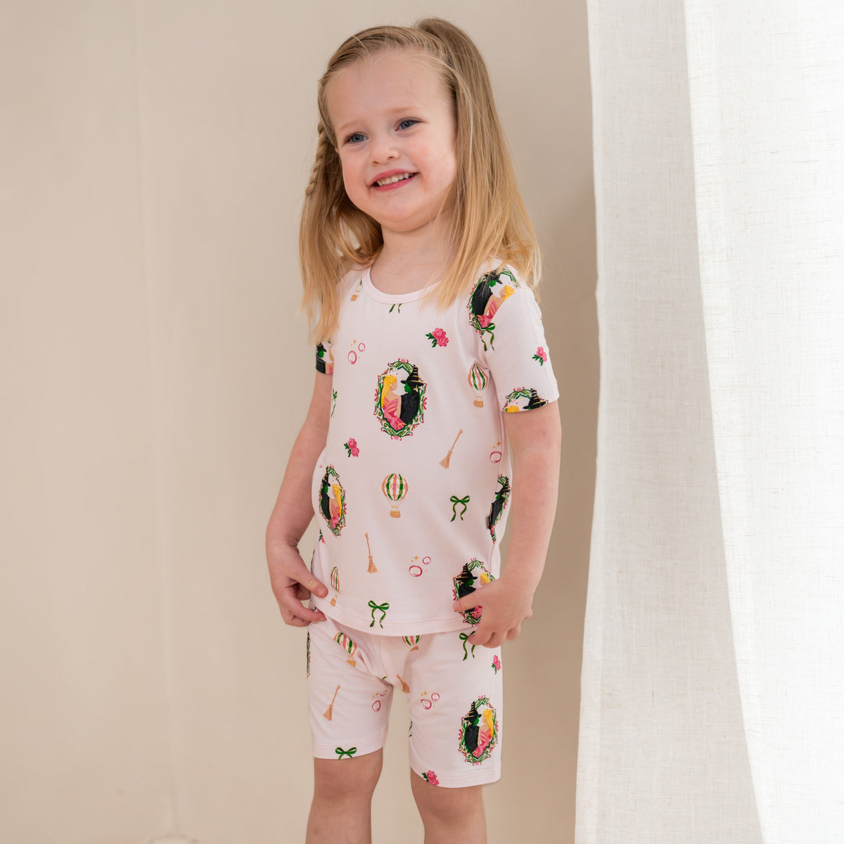 Young smiling girl standing in front of a light beige wall wearing the Short Sleeve Pajamas in Wicked