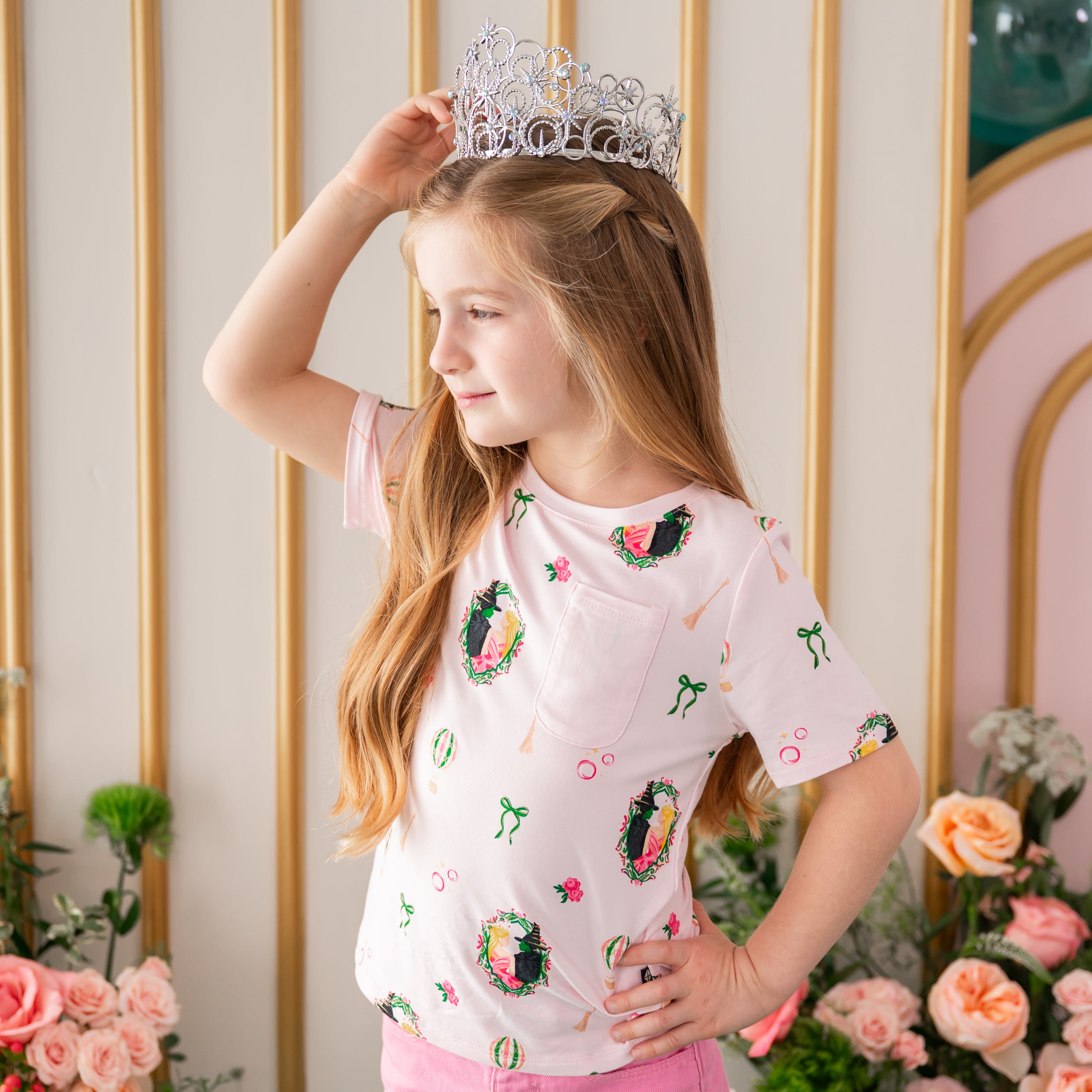 Girl posing wearing the Toddler Crew Neck Tee in Wicked with a prop tiara in front of a floral backdrop