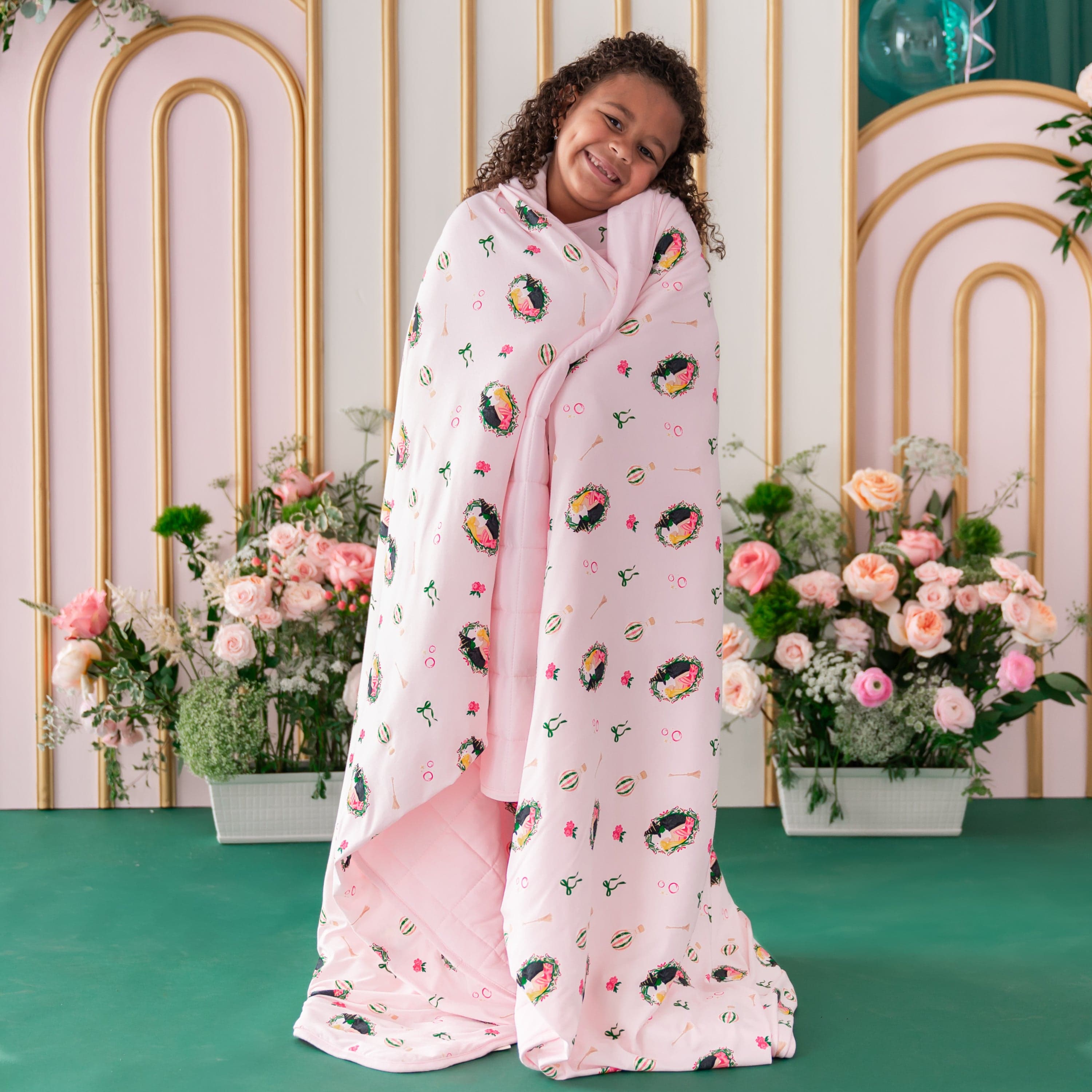 Girl standing in front of a floral backdrop with the soft and cozy Youth Blanket in Wicked 2.5 around her shoulders