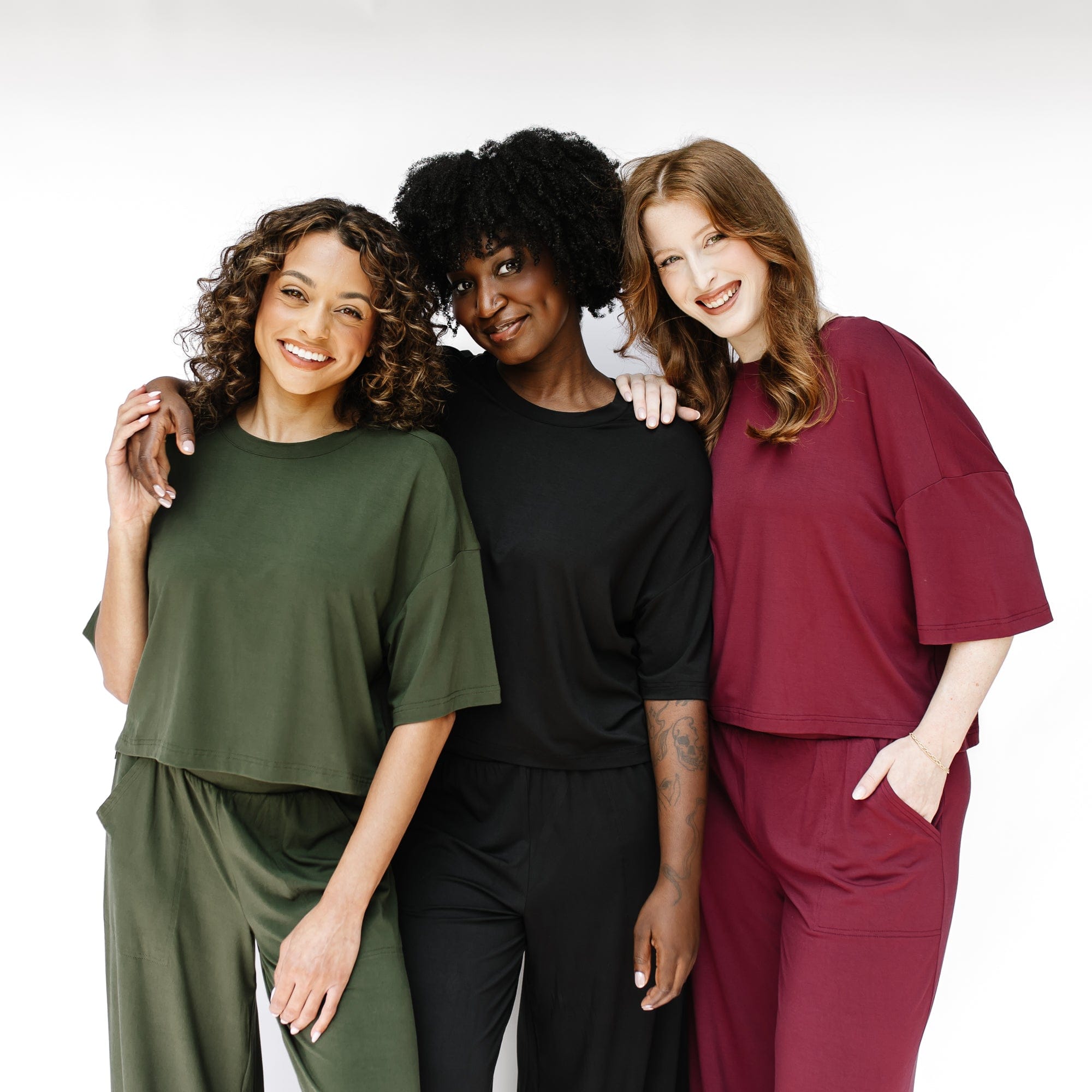 Three models standing side by side wearing the Women's Short Sleeve Tee in Burgundy, Midnight and Fir with matching wide leg pants