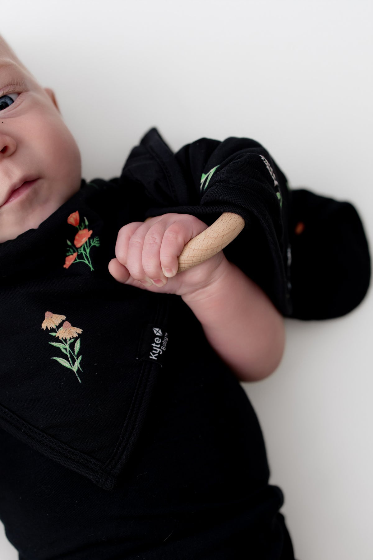 Baby wearing black bodysuit holding Lovey in Midnight Wildflower with Removable Wooden Teething Ring on a white background