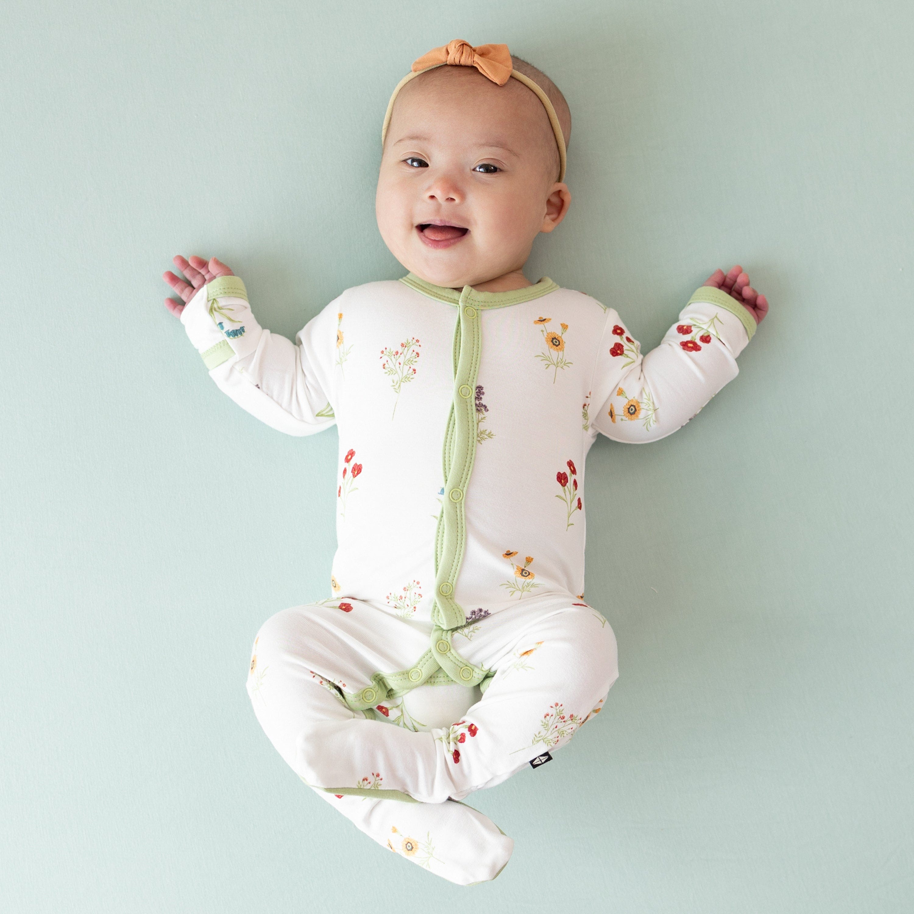 Baby smiling wearing Footie in Wildflower with legs scrunched up