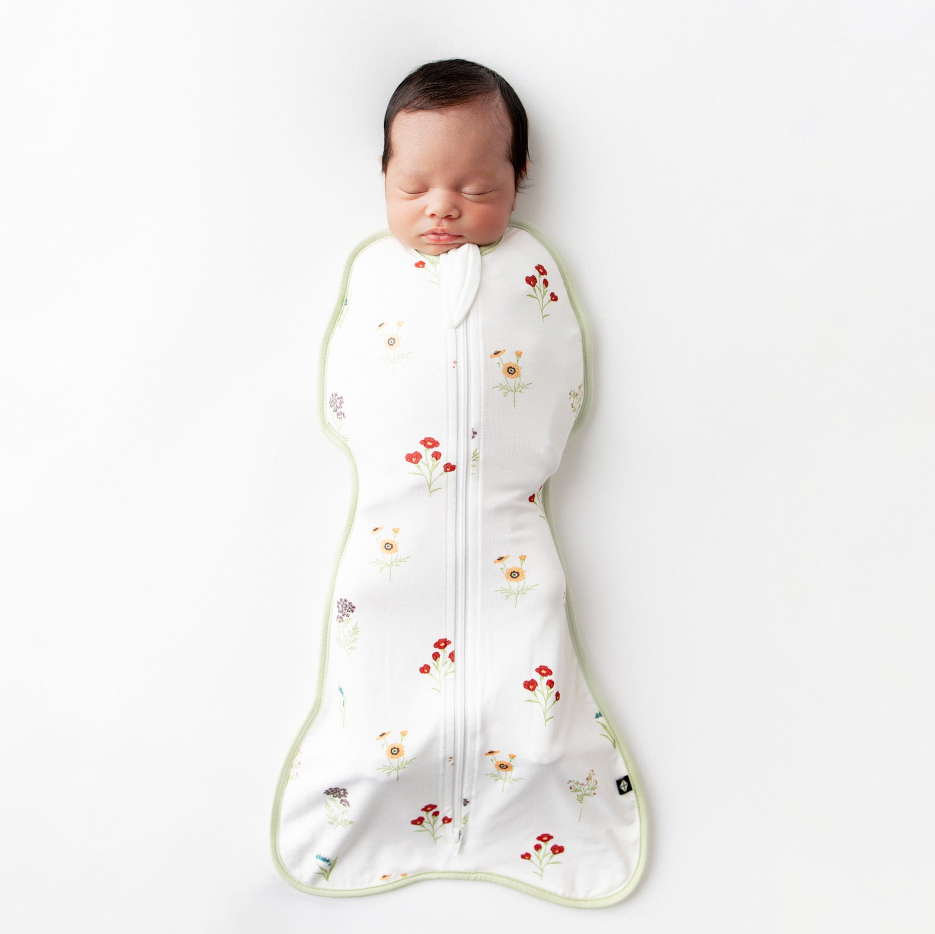 Sleeping newborn laying on a light neutral surface wearing the Swaddle Bag in Wildflower 0.5
