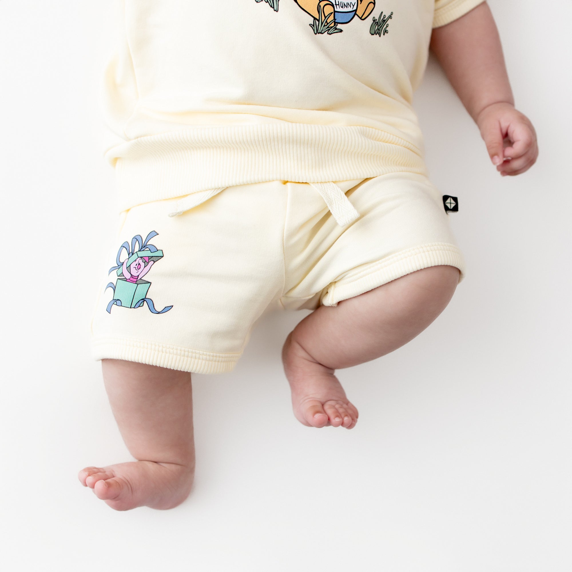Close up of the shorts of the Short Sleeve Jogger Set in Winnie the Pooh on Chamomile shown on an infant laying on a white surface