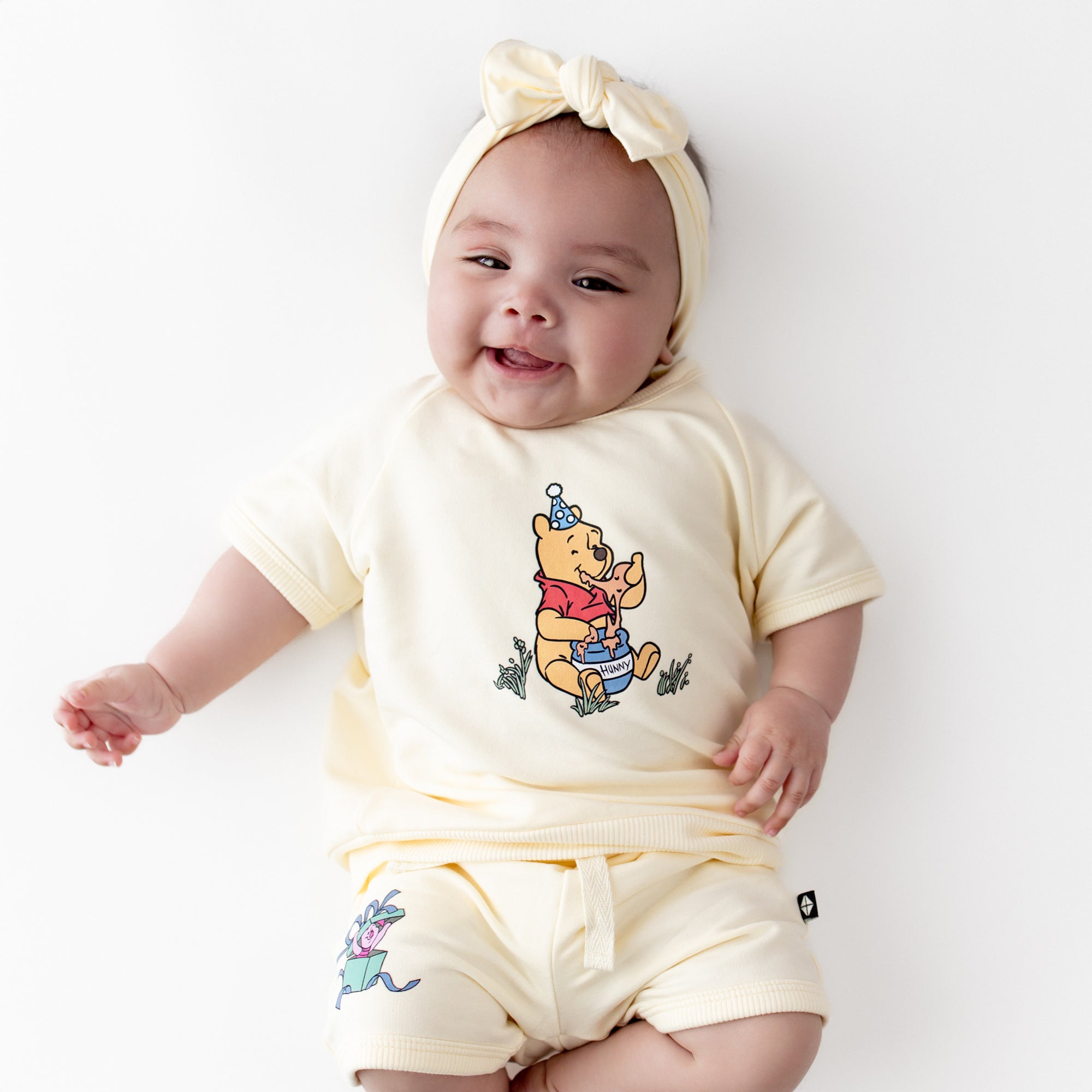 Short Sleeve Jogger Set in Winnie the Pooh on Chamomile shown on an infant wearing a matching light yellow bow
