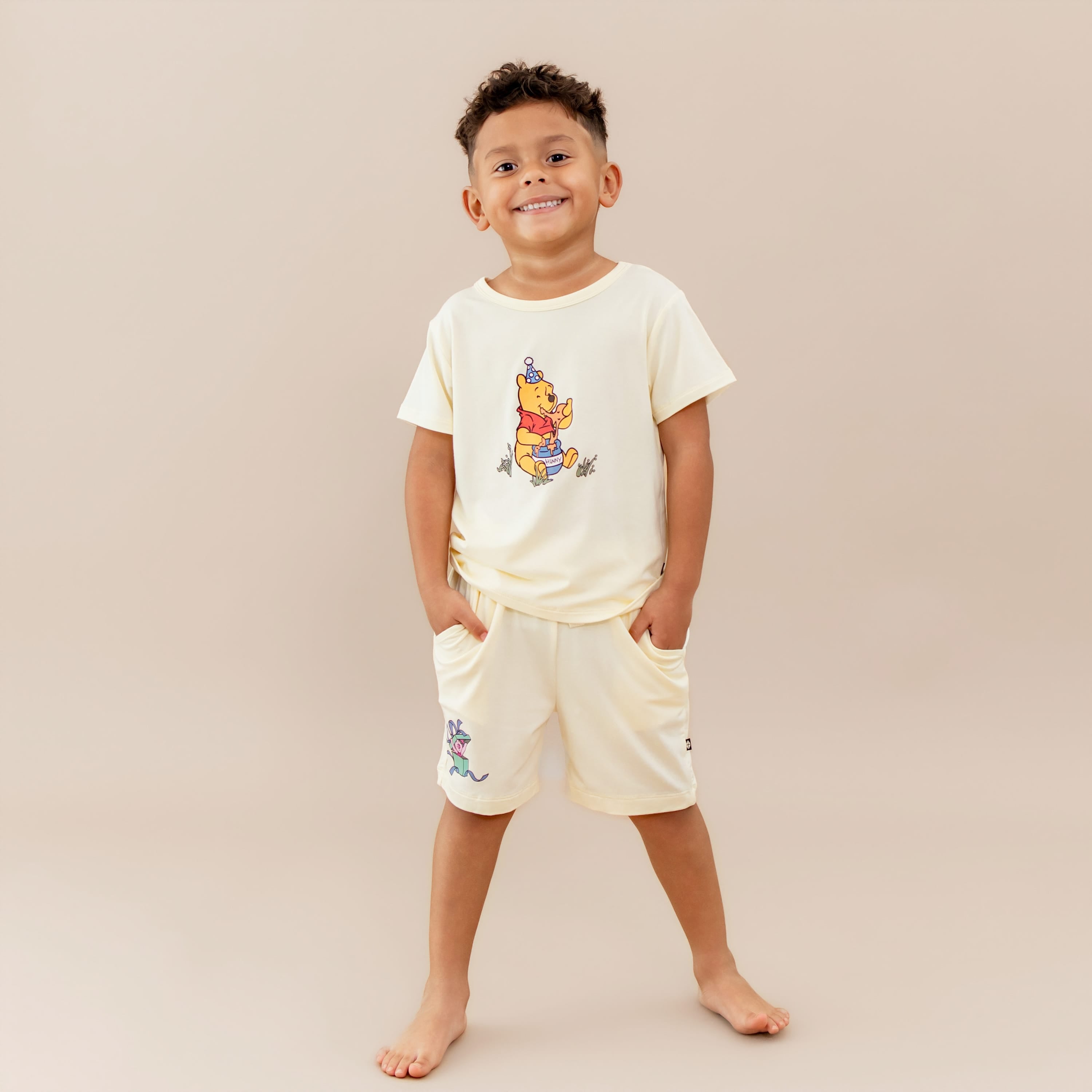 Young smiling boy wearing the Toddler Basic Tee in Winnie the Pooh on Chamomile paired with the Winnie the Pooh drawstring shorts on chamomile
