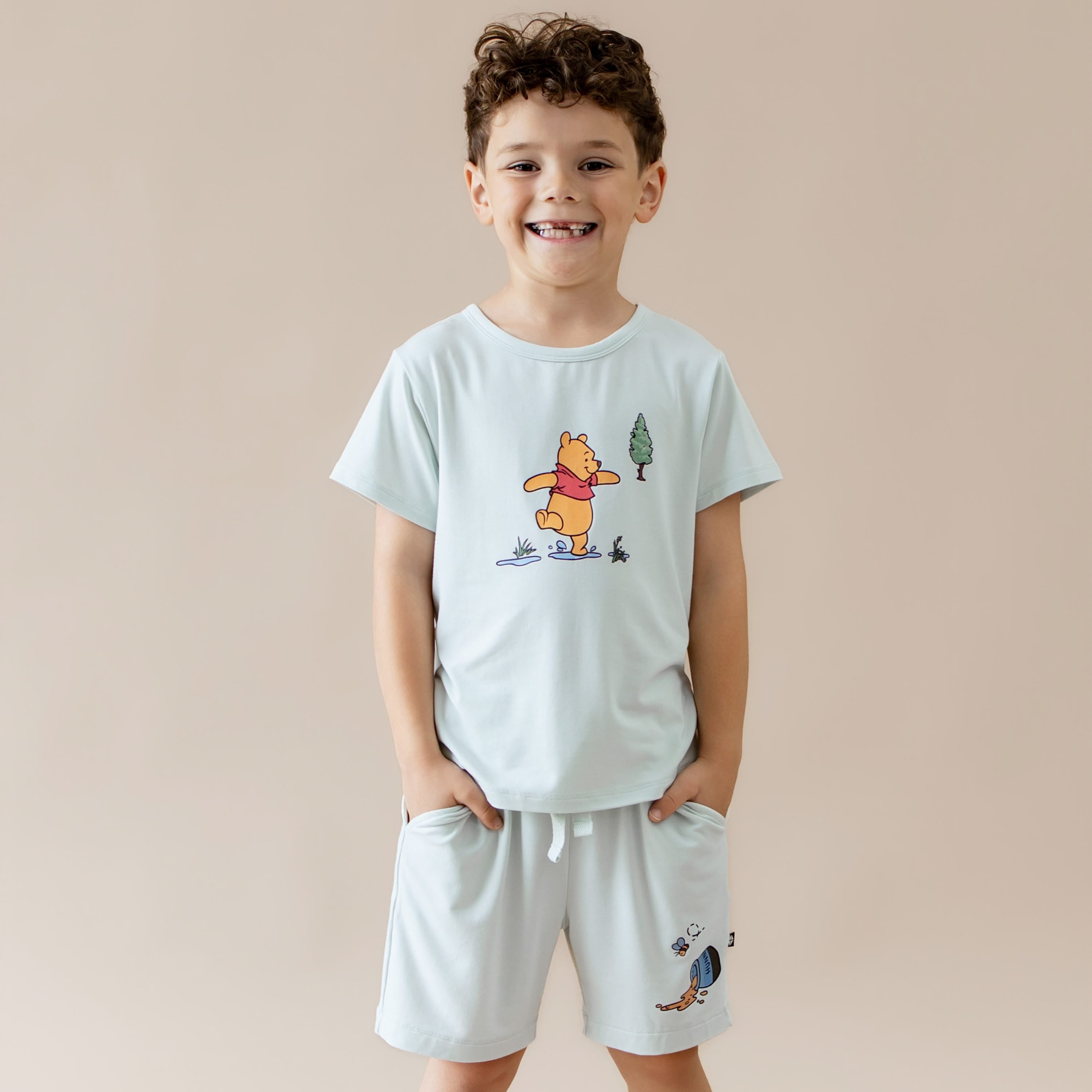 Young smiling boy modeling the Toddler Basic Tee in Winnie the Pooh on Dew paired with the matching drawstring shorts